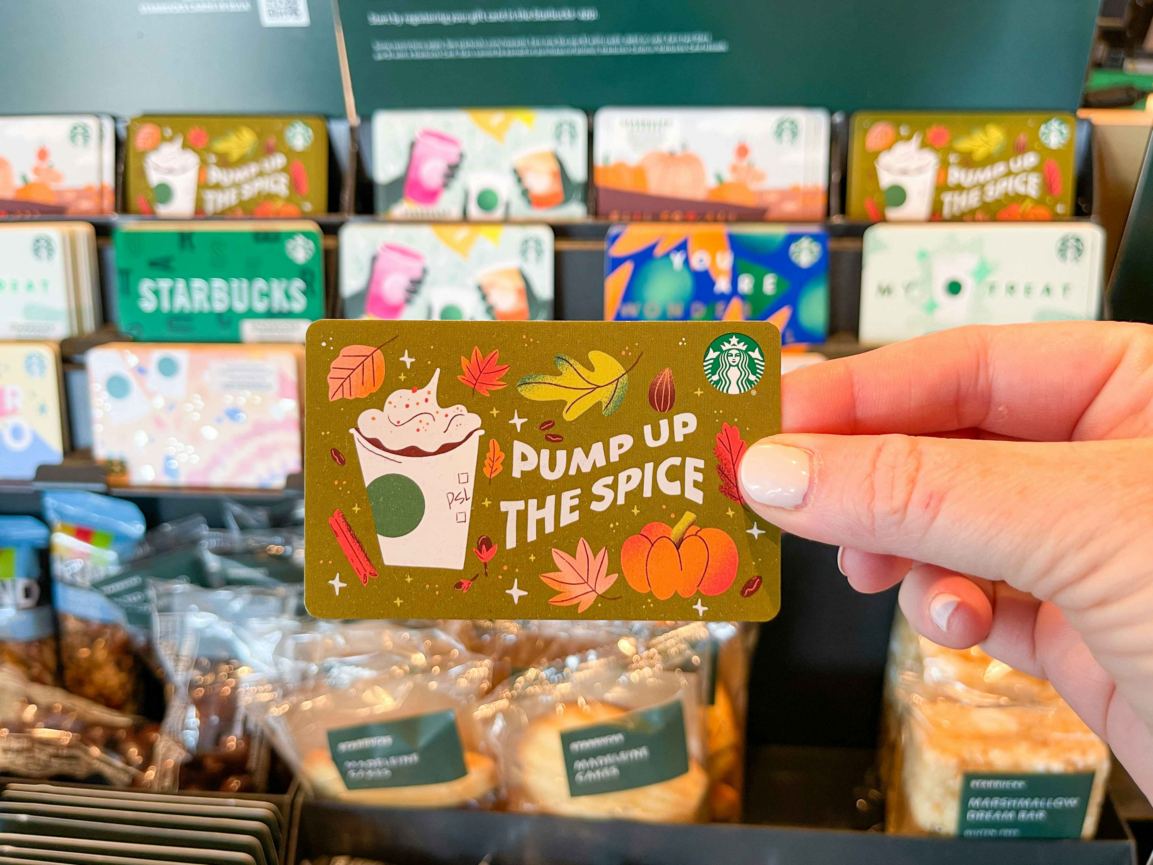 person holding fall-themed starbucks gift card near checkout