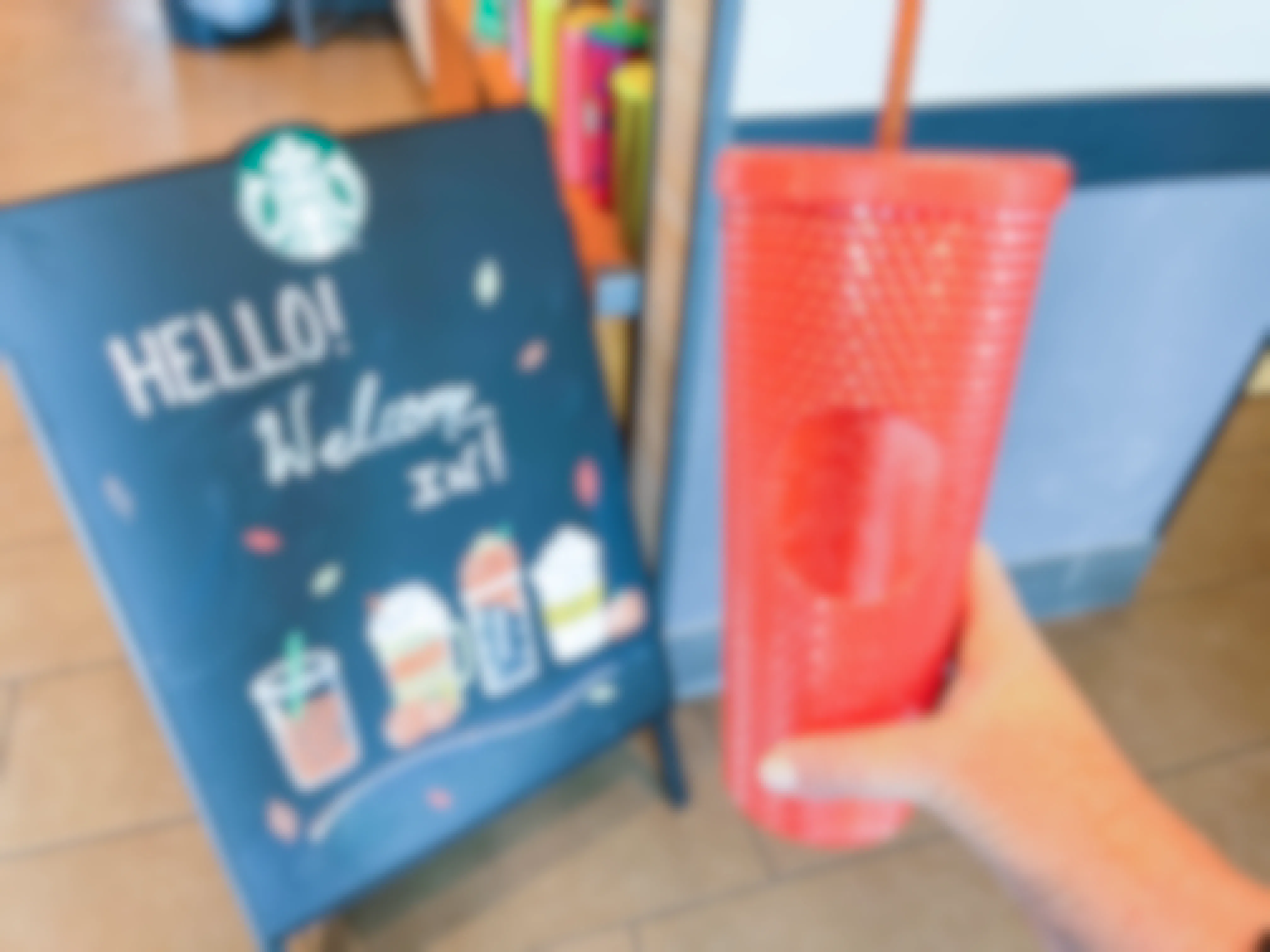 A person holding up a reusable Starbucks cup near a "welcome in" sign.