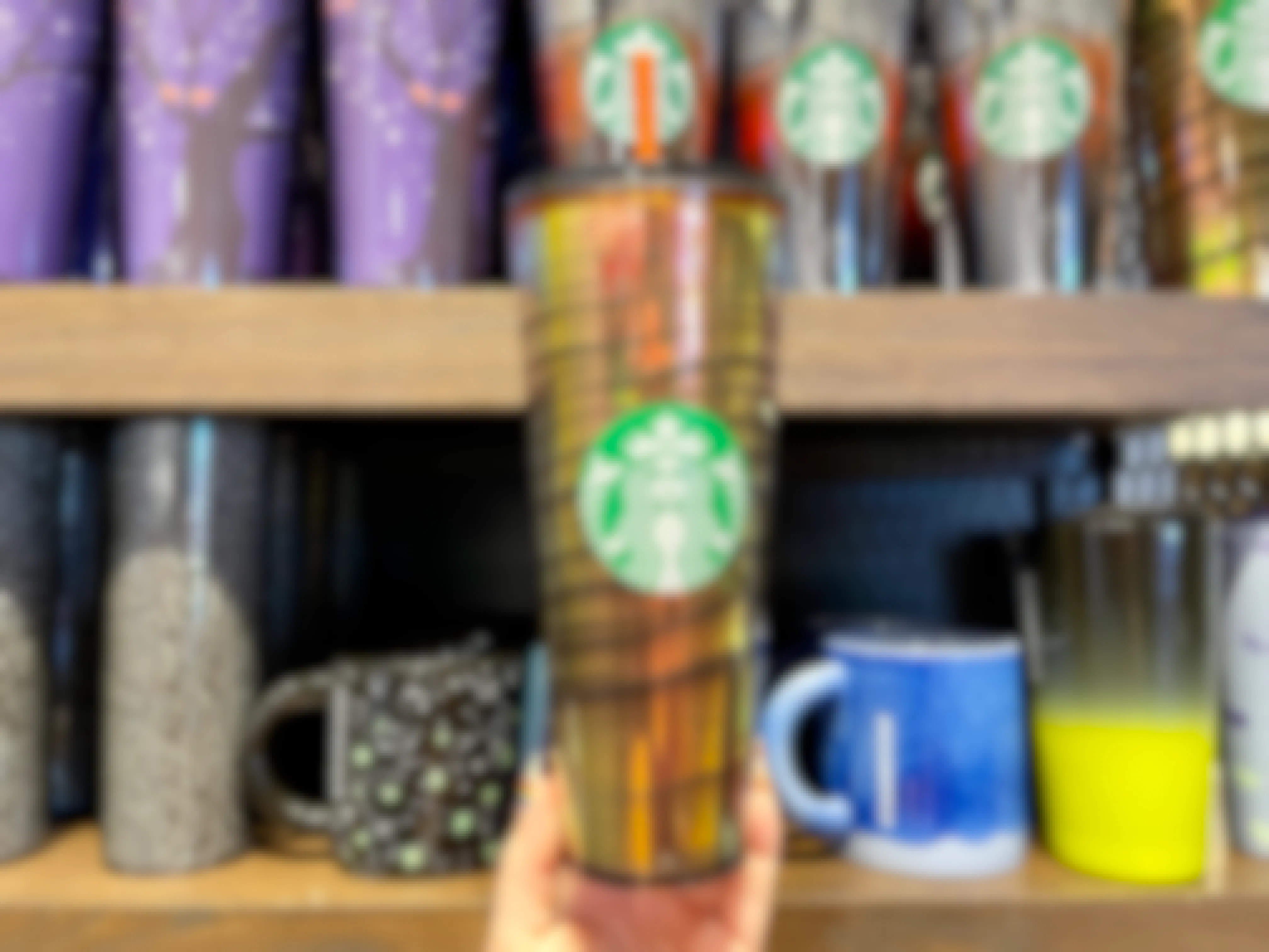 A person holding a Starbucks cup from the new Halloween release in front of a shelf of other Starbucks cups.