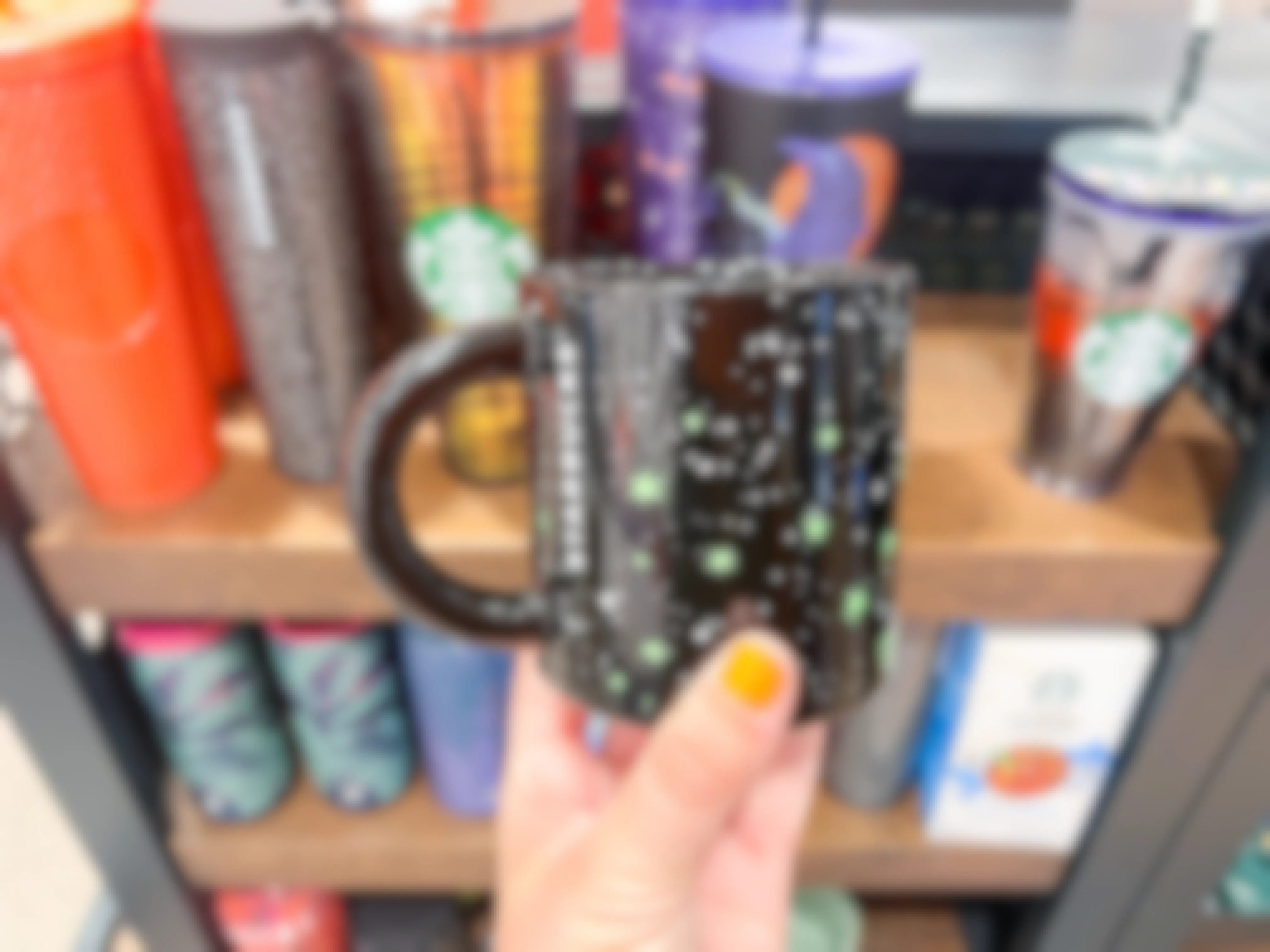 A person holding up a Starbucks mug in front of a shelf.