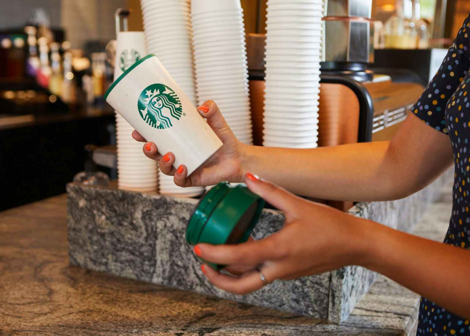 A person holding a Starbucks personal reusable cup at the cafe counter.