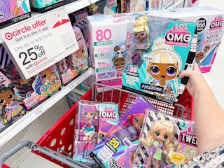 A person holding an LOL Surprise doll over a cart full of more dolls next to a sign for the Target Toy Book sale for 25% off a toy or book.