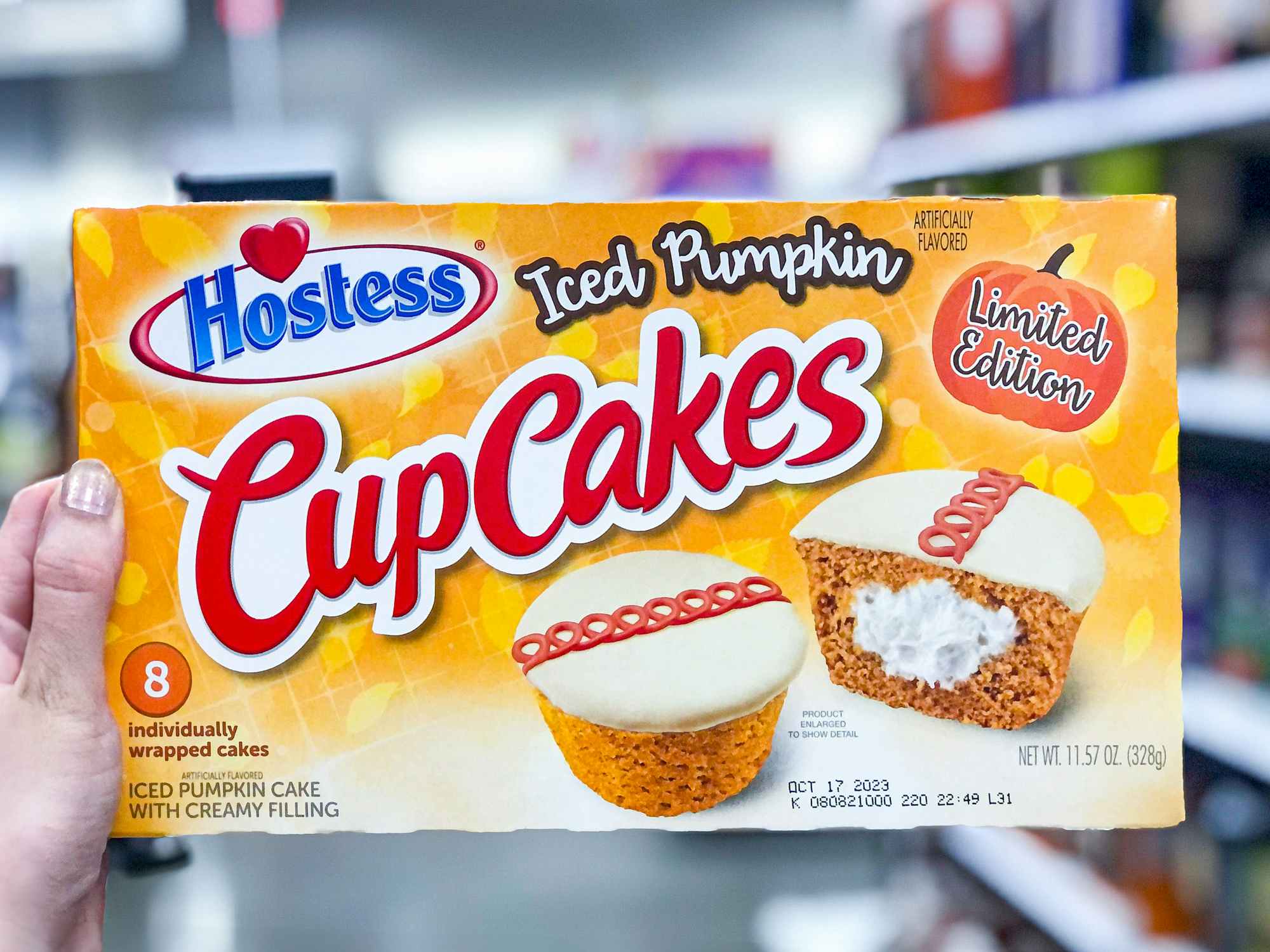 someone holding up a box of Hostess iced pumpkin cupcakes