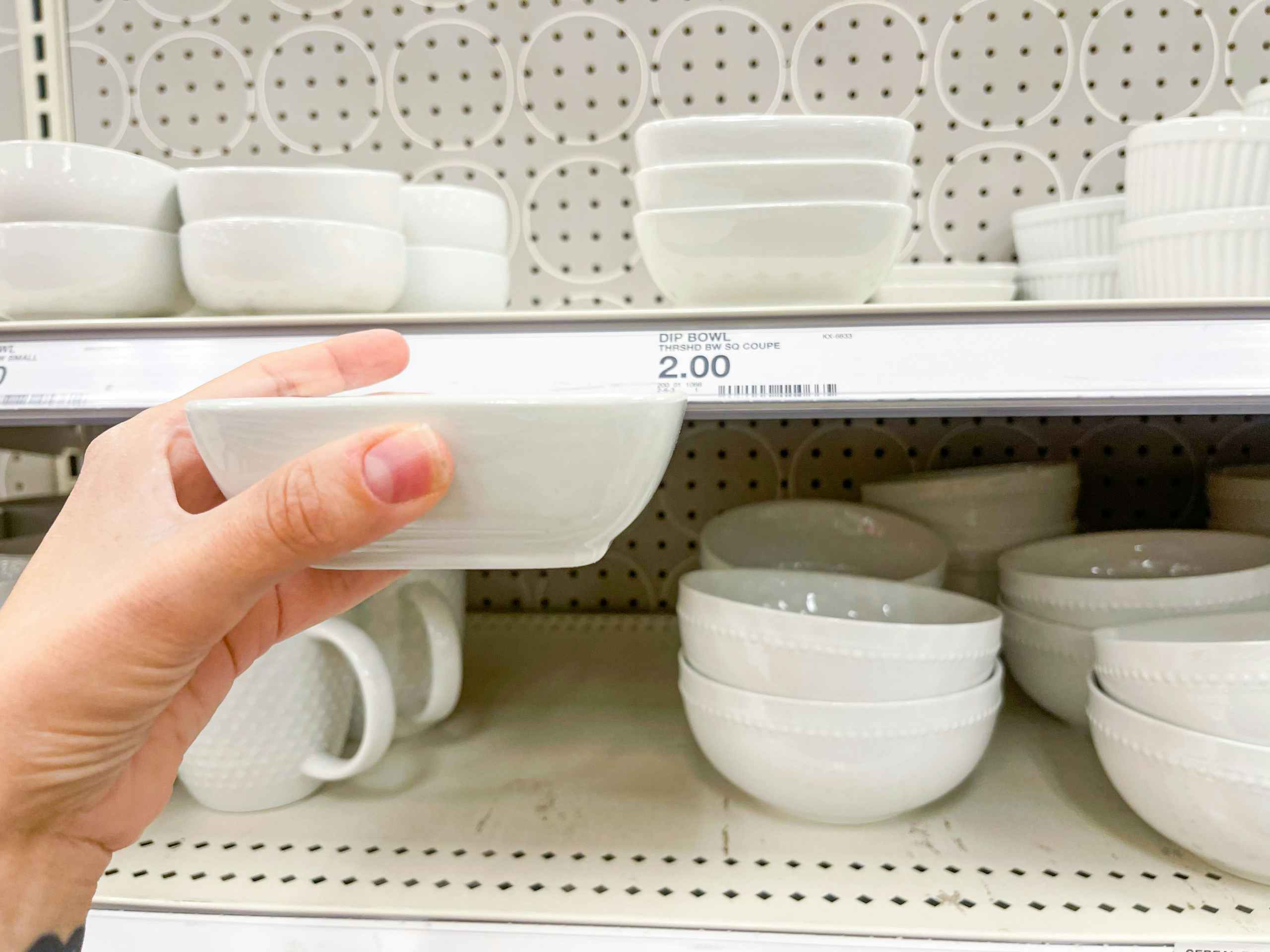 Hey small dipping bowl held up by hand in front of a store shelf with other bowls and plates on it.