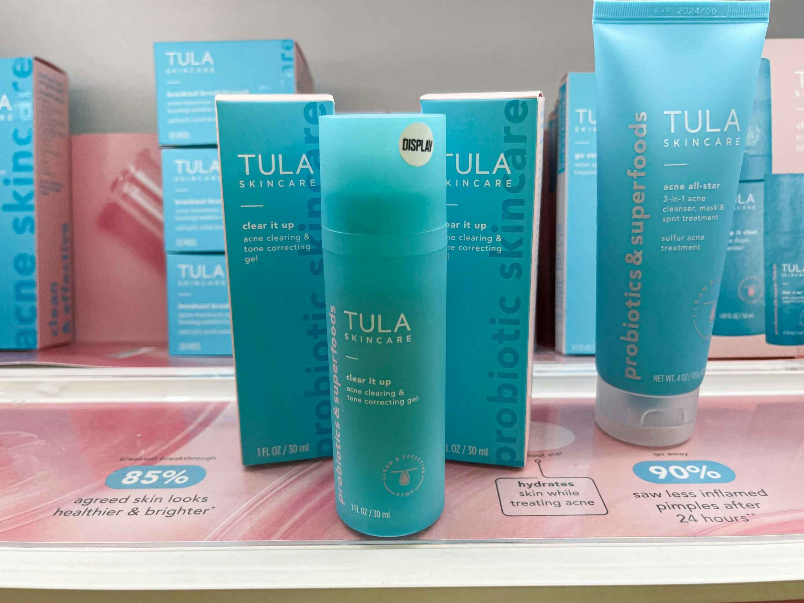 A bottle of Tula skincare clear it up acne clearing and tone correcting gel sitting on a store shelf with two boxes of Tula skincare clear it up acne clearing and tone correct in gel behind it.