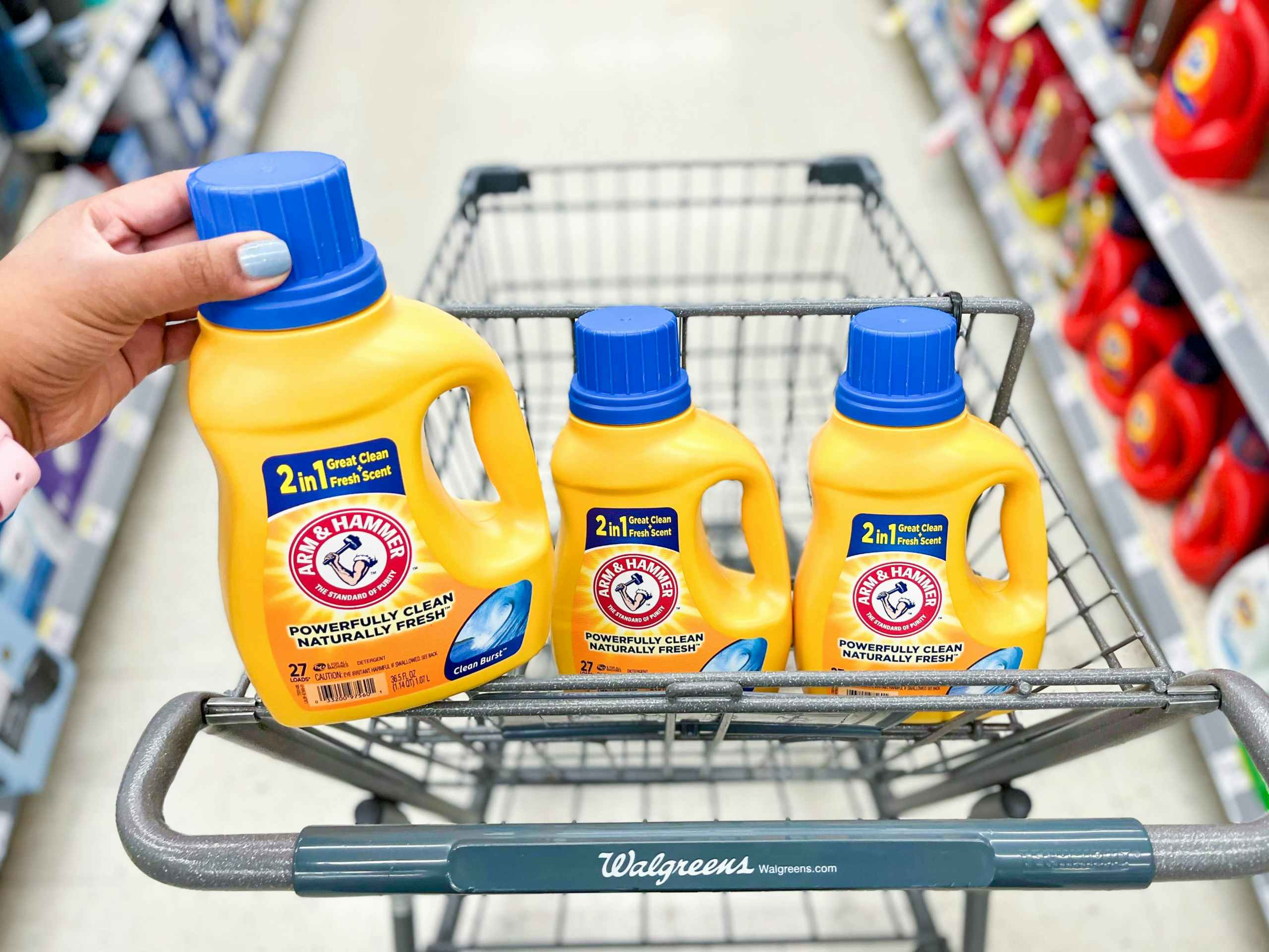hand on bottle of Arm & Hammer Liquid detergent sitting on cart next to two other bottles