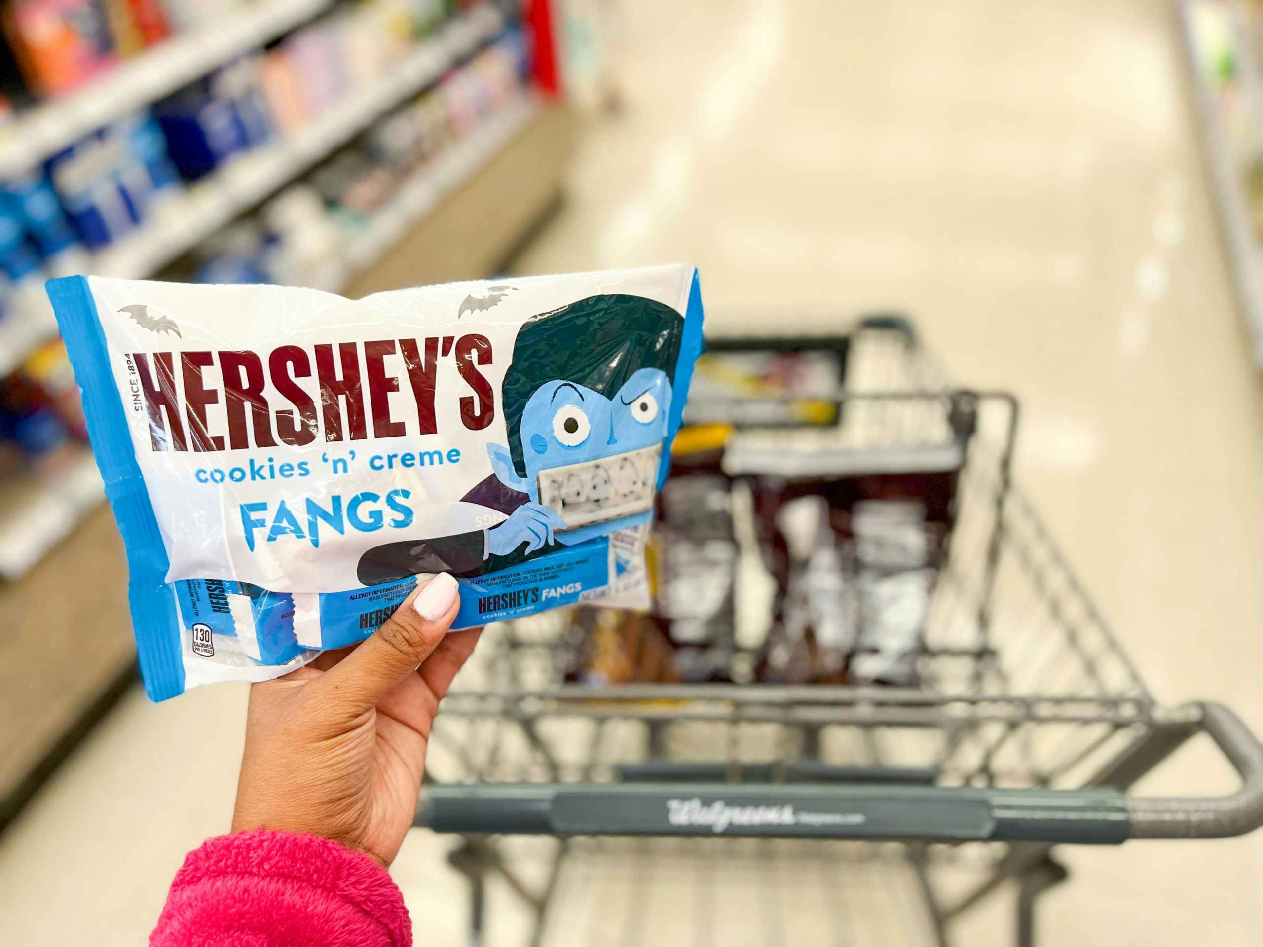 hand holding a snack size bag of Hershey's cookies n creme fangs in front of shopping cart with two bags of Hershey's chocolates inside