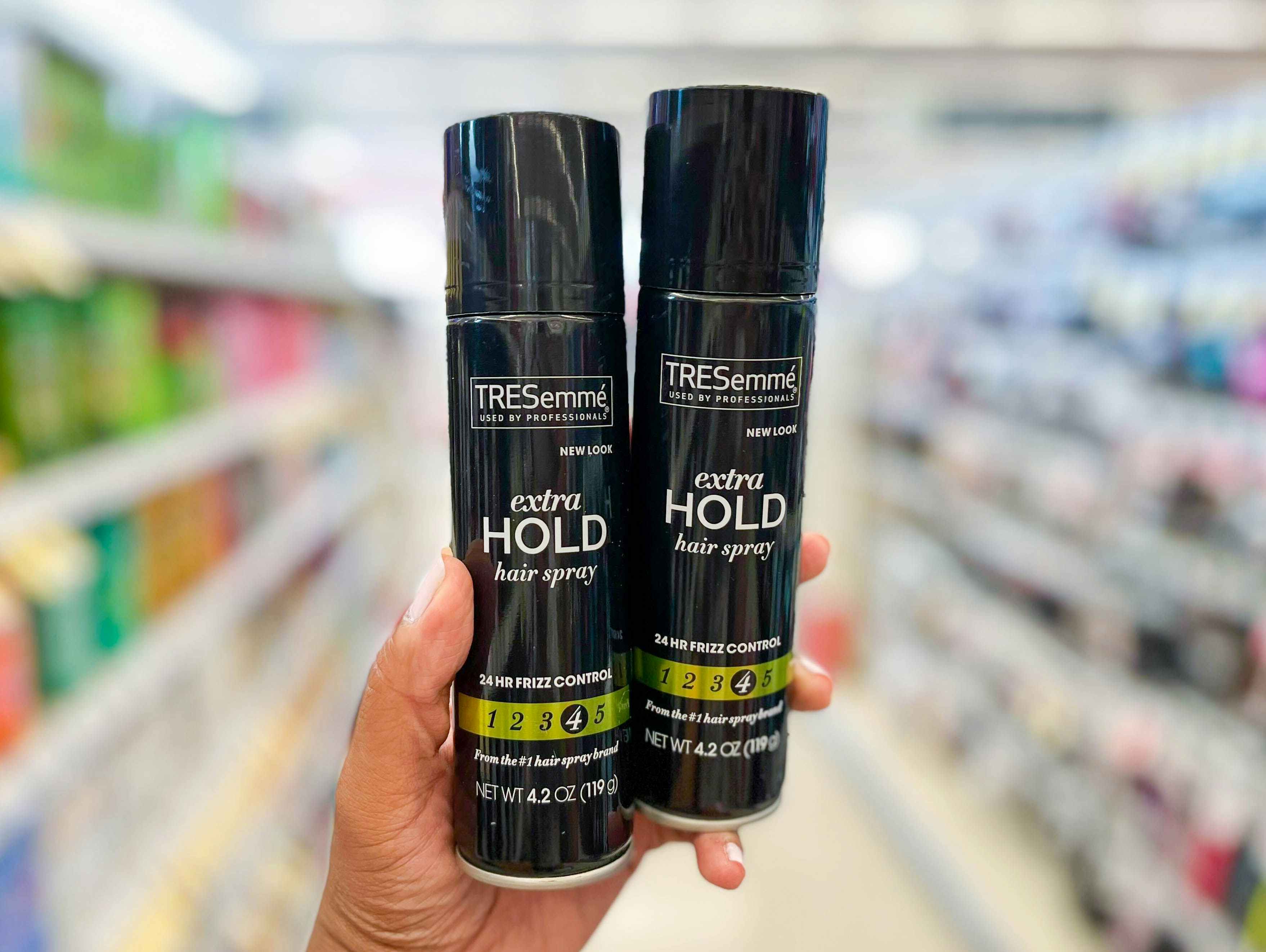 hand holding two cans of Tresemme hair spray in aisle