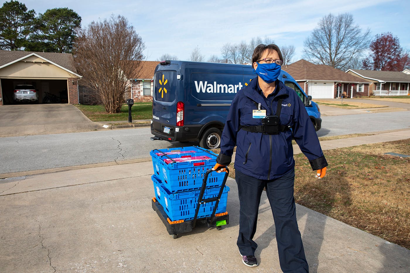 A Walmart employee walking up a house with a cart filled with groceries.