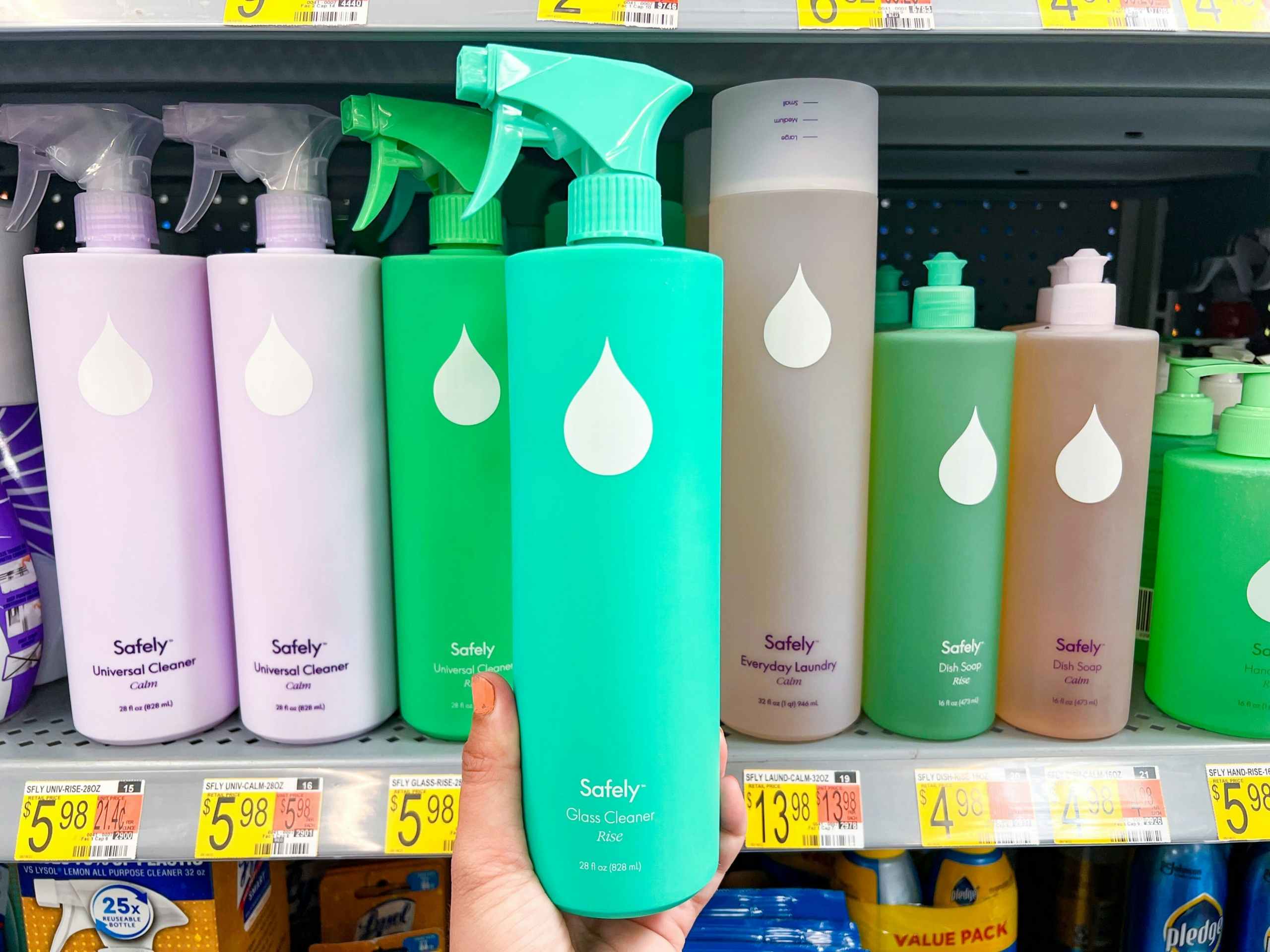 hand holding a blue bottle of Safely glass cleaner in front of a shelf with like items