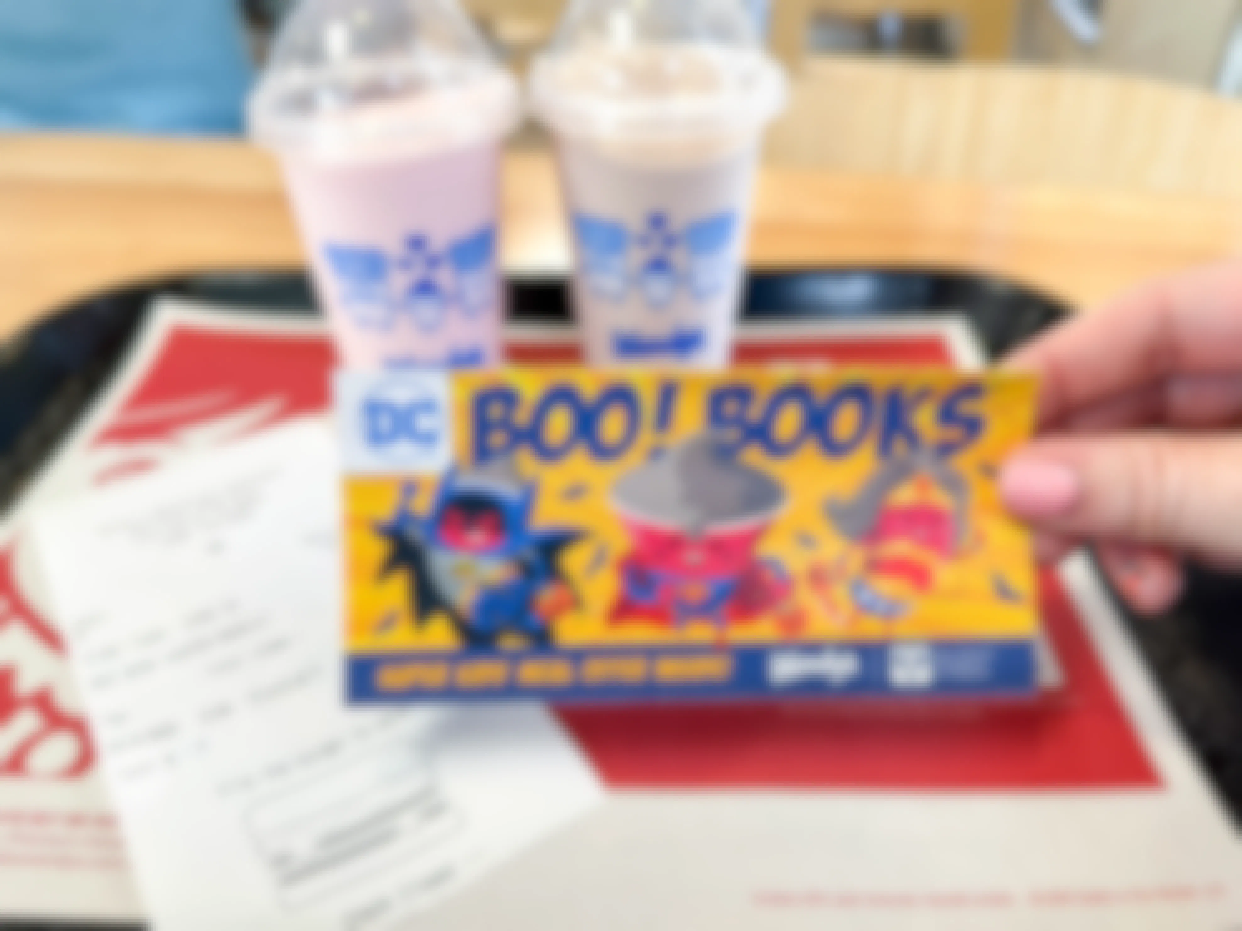 a person holding a wendys boo books in front of two frostys and receipt on tray 