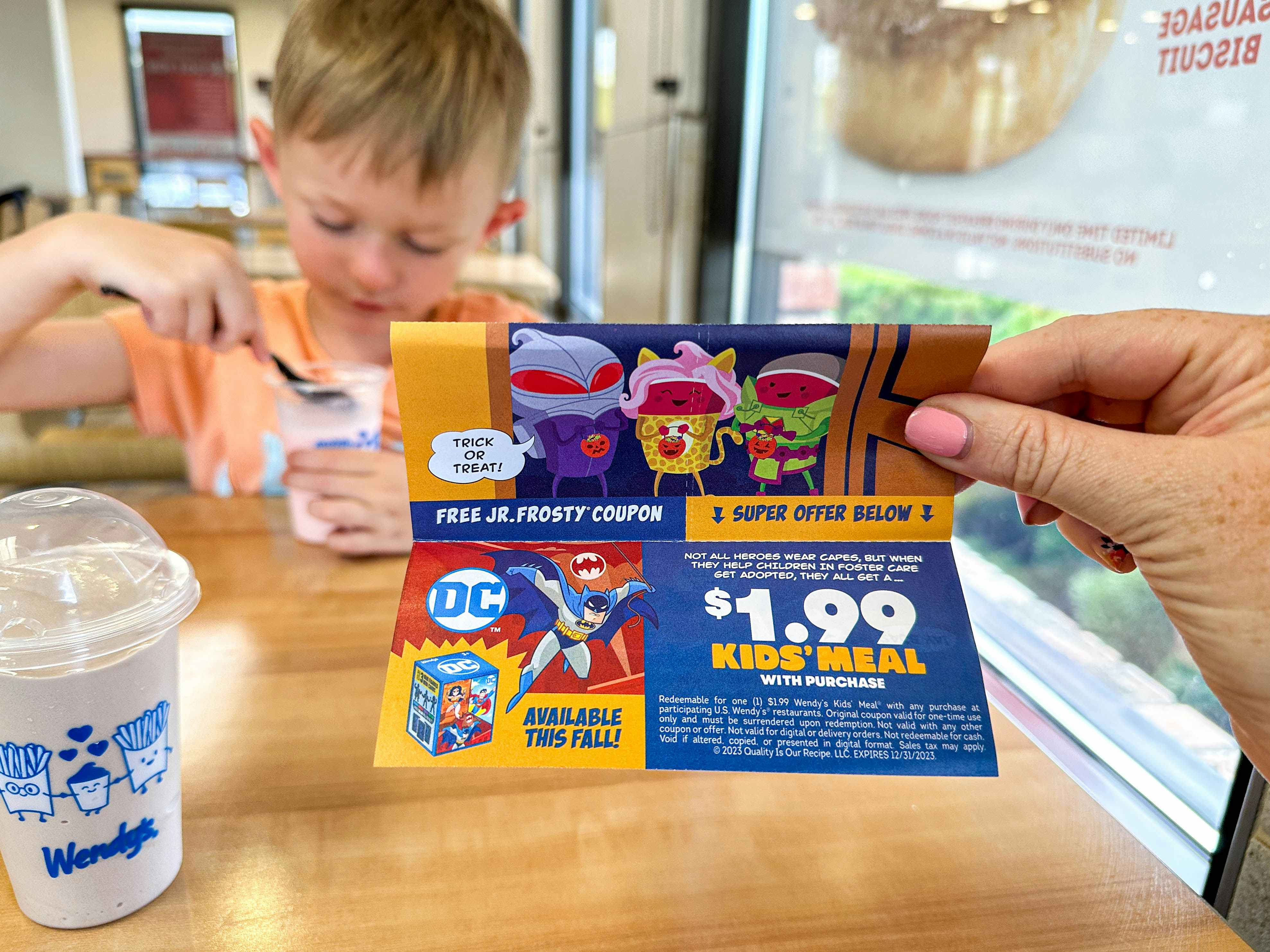 a wendys boo book coupon for discount kids meal being held in front of child eating 