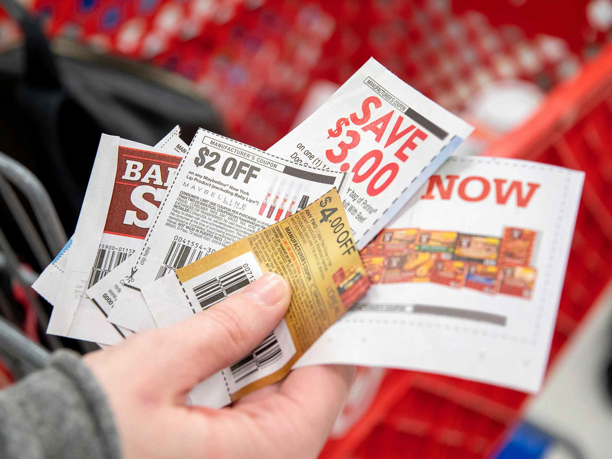 persons hand holding several coupons near target shopping cart