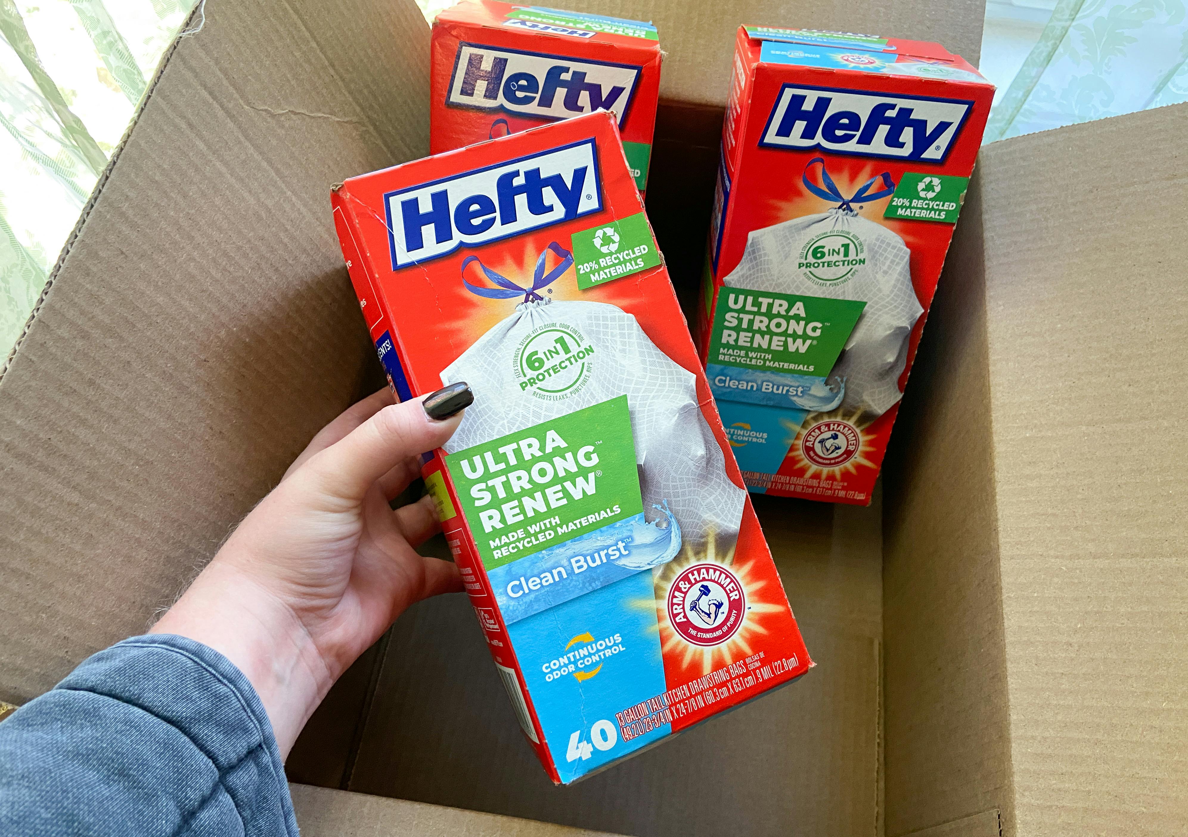 Hand holding a box of hefty ultra strong trash bags over an amazon box