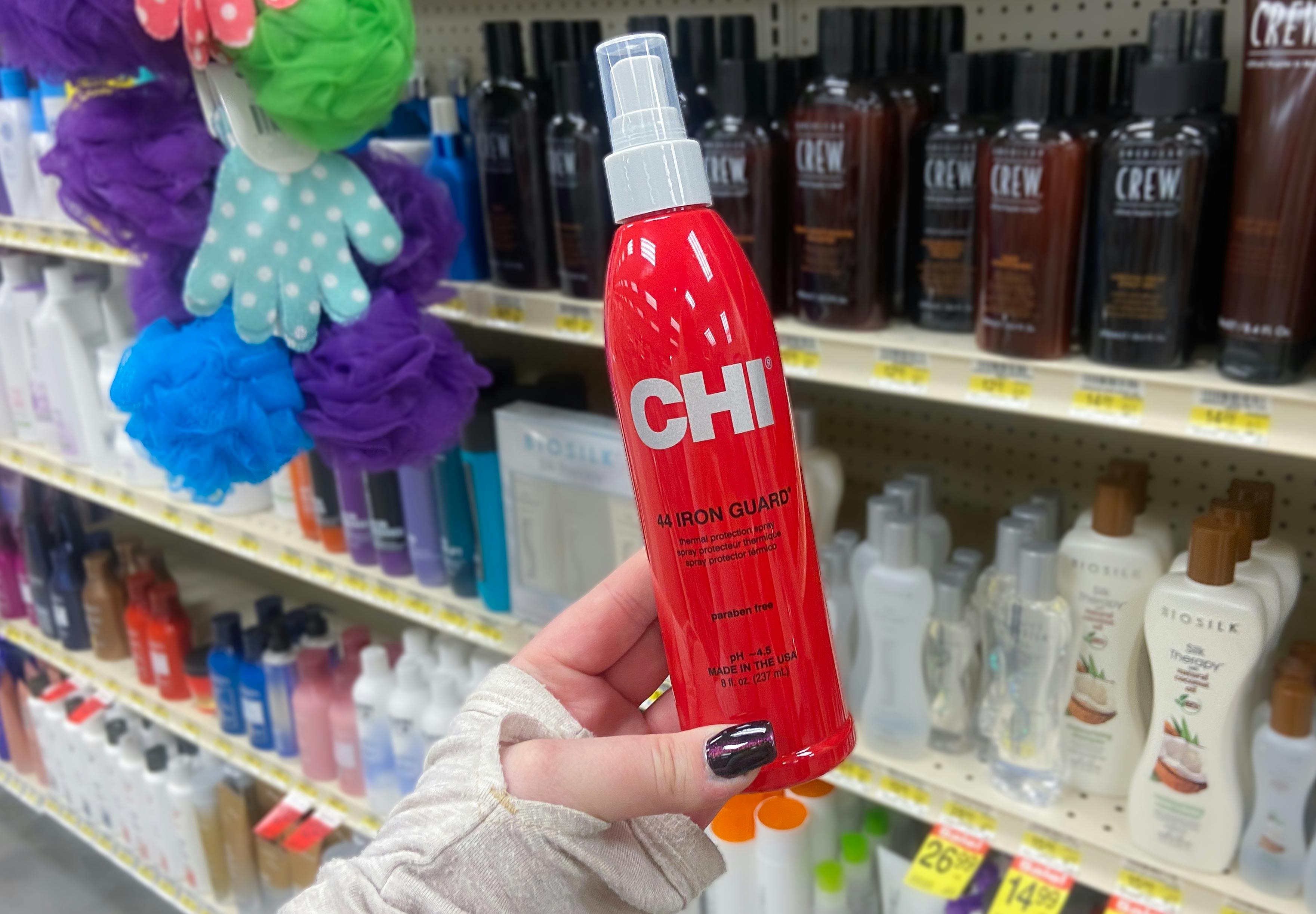 a hand holding a bottle of chi iron guard heat protectant hair spray in a store aisle