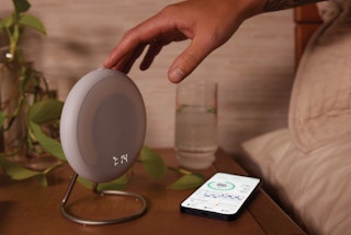 A person's hand reaching for a Halo Rise on the nightstand