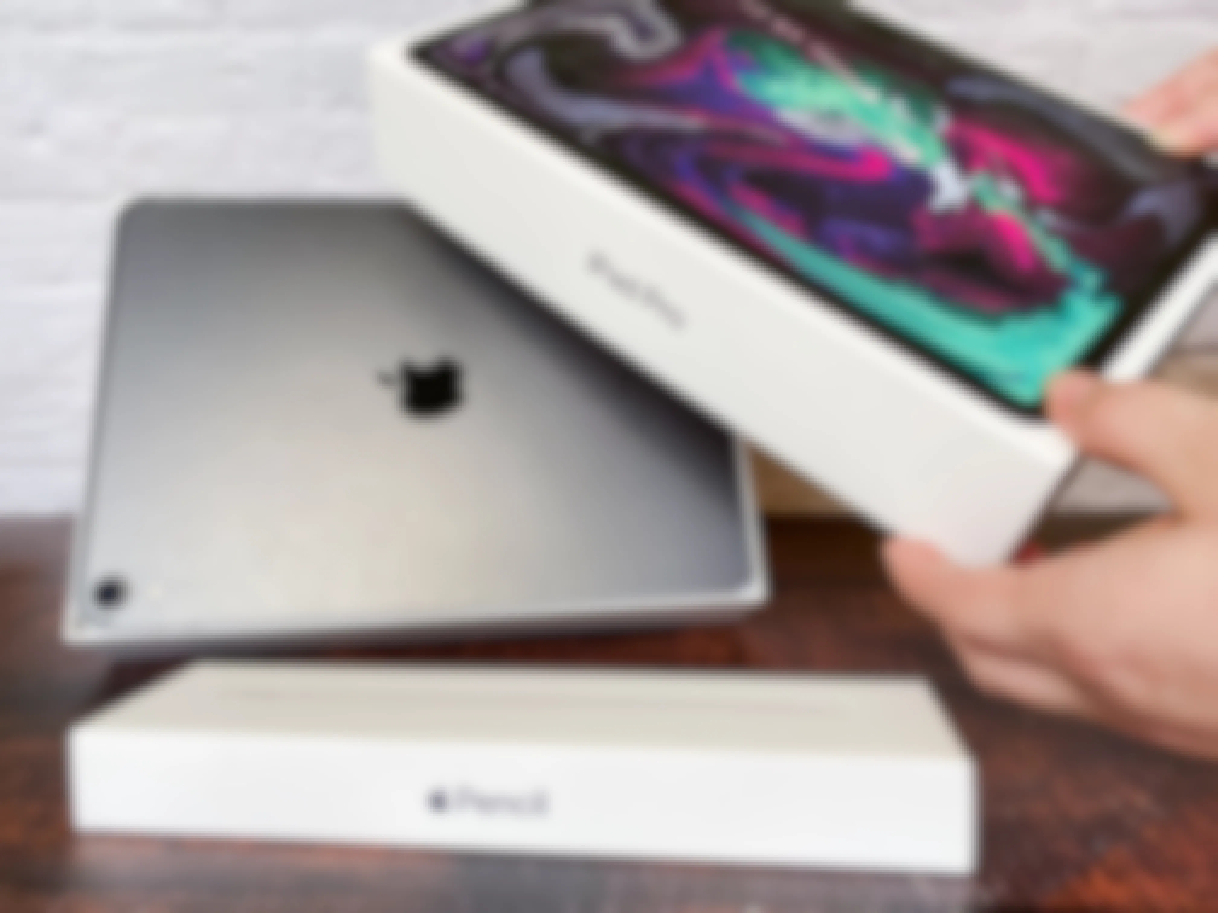 A person opening an iPad pro box sitting on a table with an Apple pencil box.