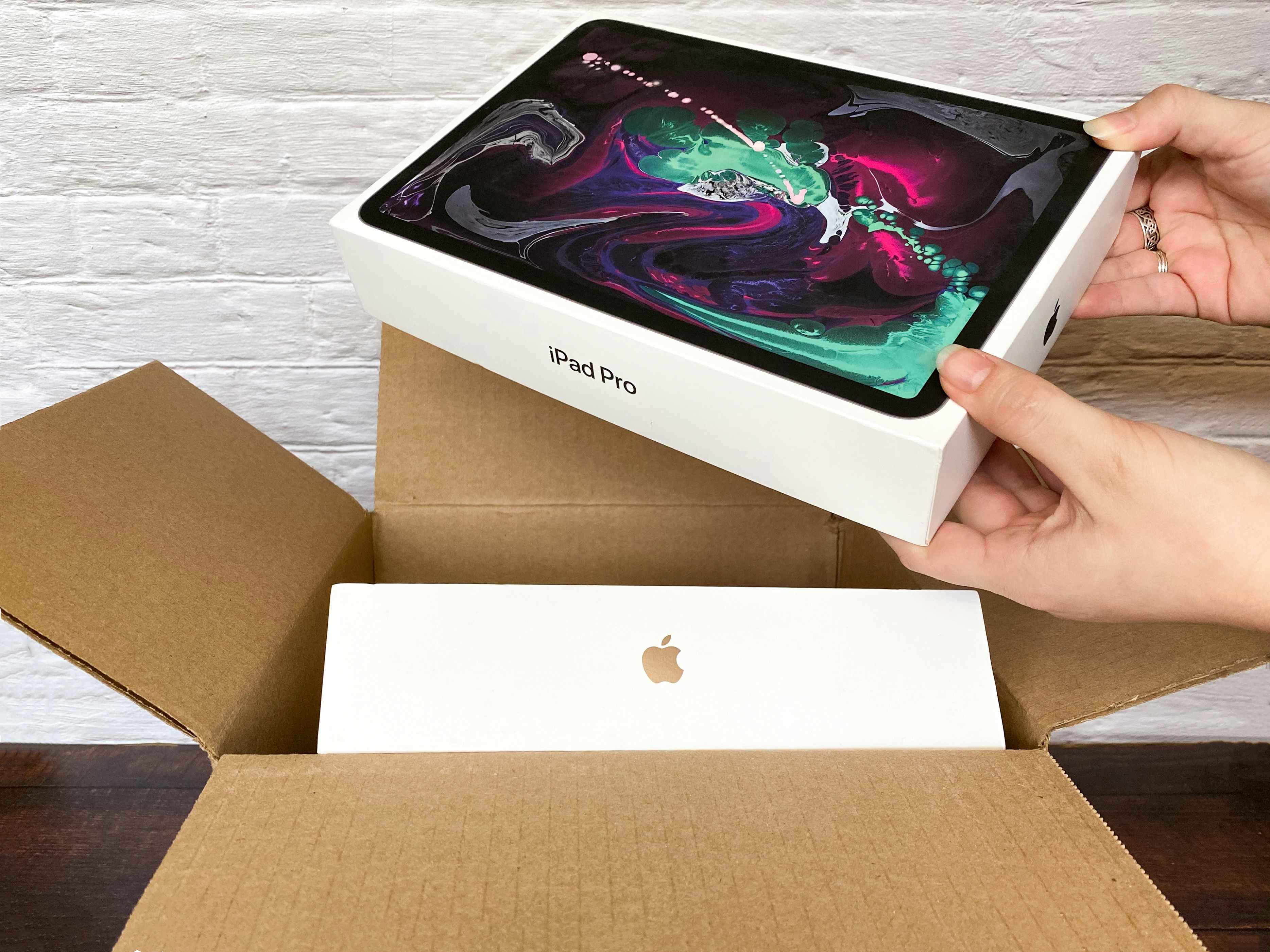 A person taking an iPad pro out of a shipping box with another Apple product inside.