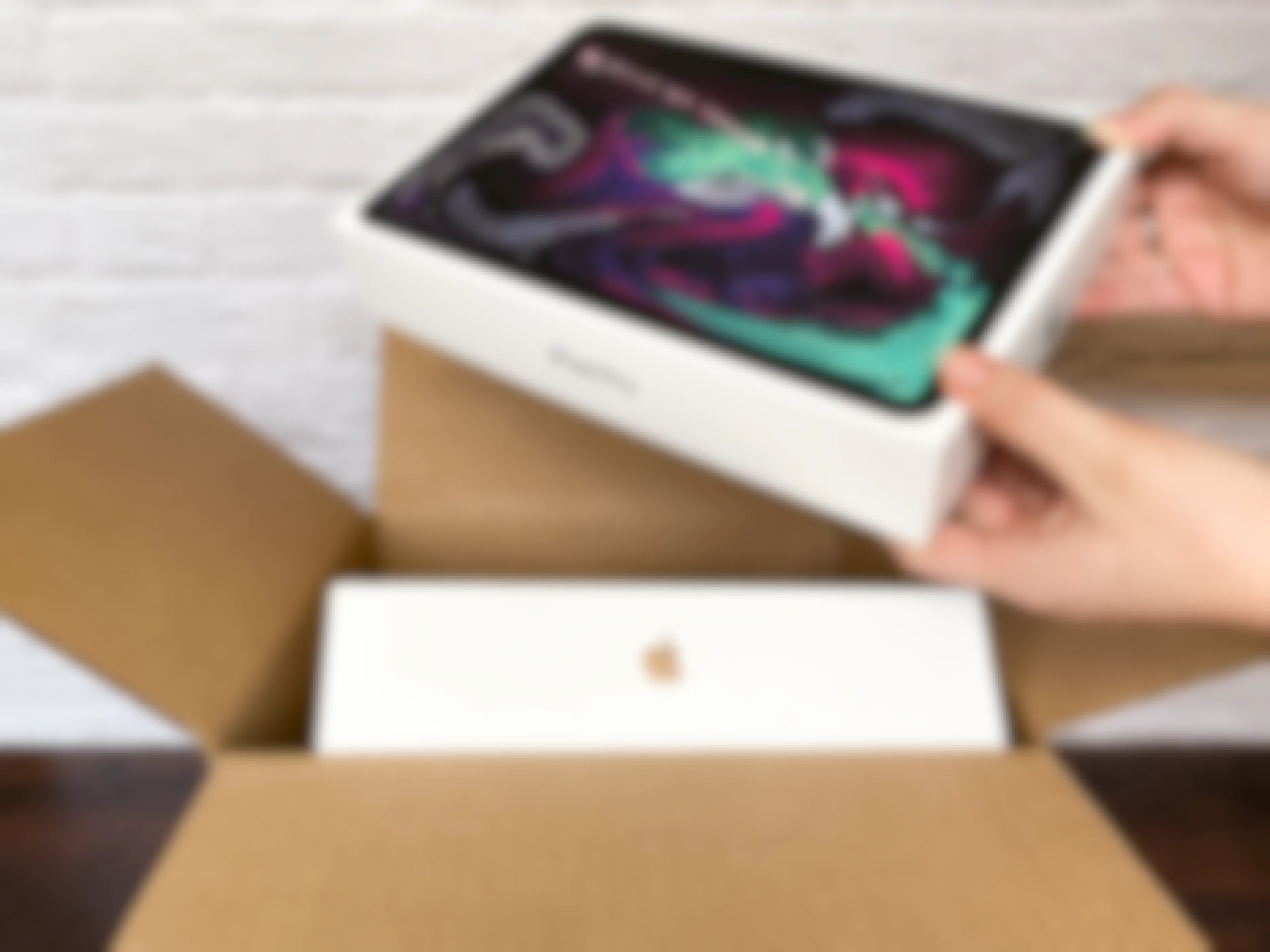 A person taking an iPad pro out of a shipping box with another Apple product inside.