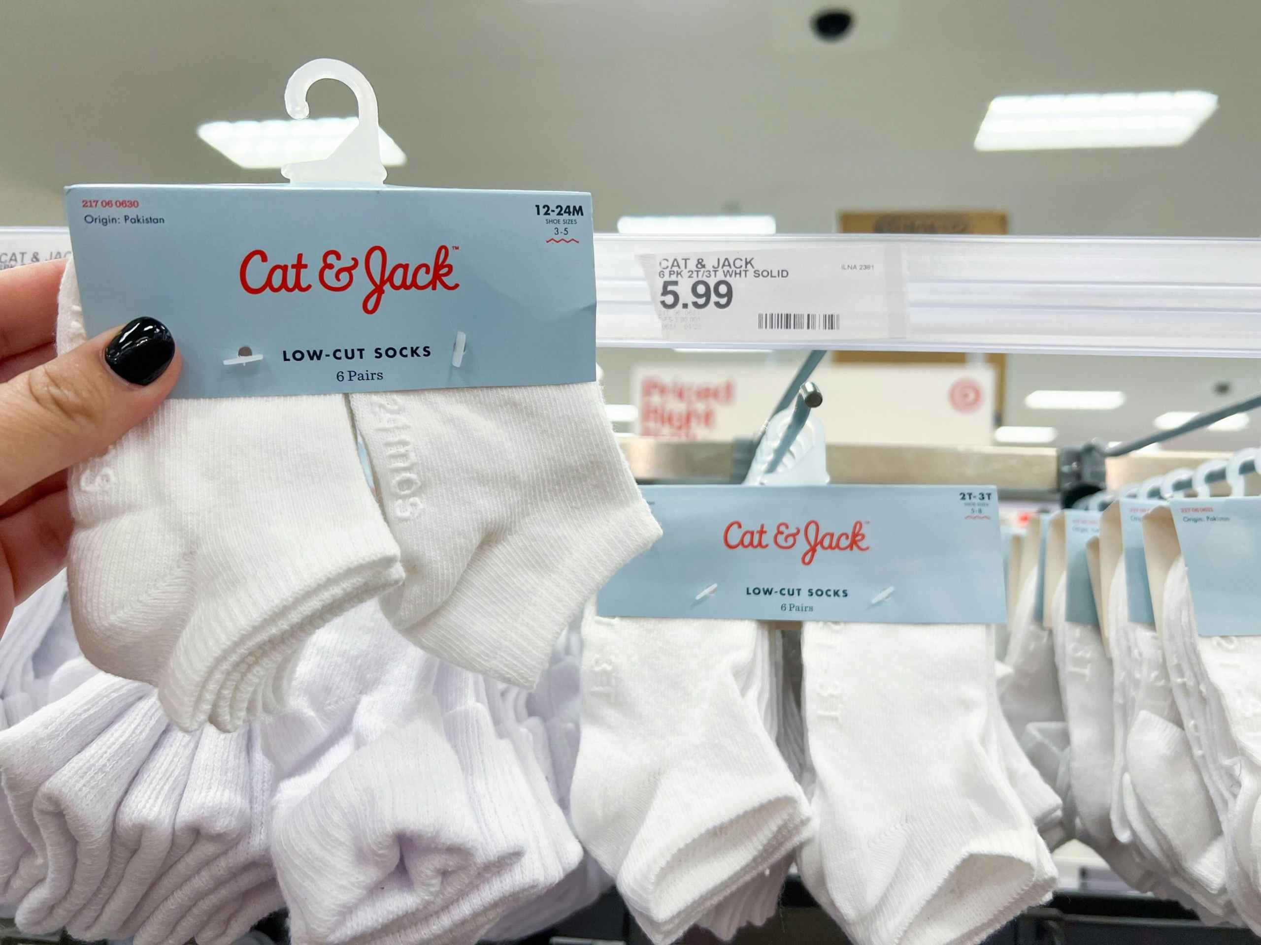 A hand holding a six pack of baby socks in front of other socks