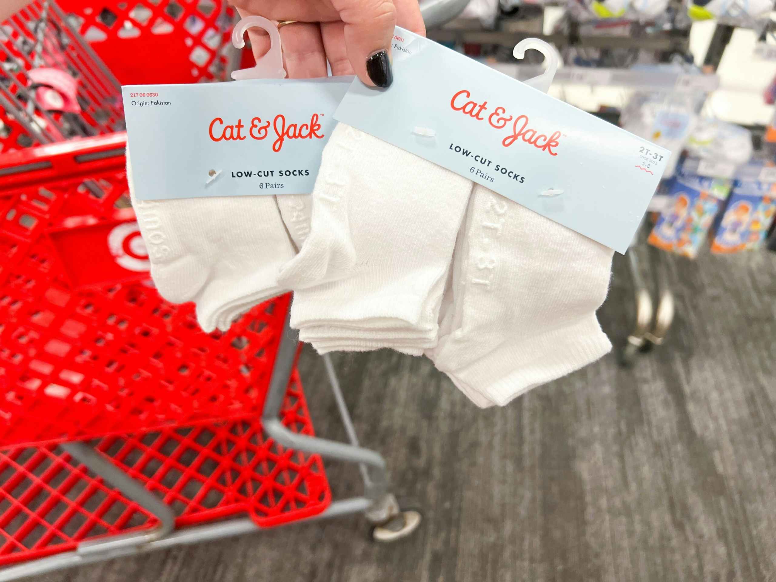 Hand holding two sets of baby socks in front of a Target cart