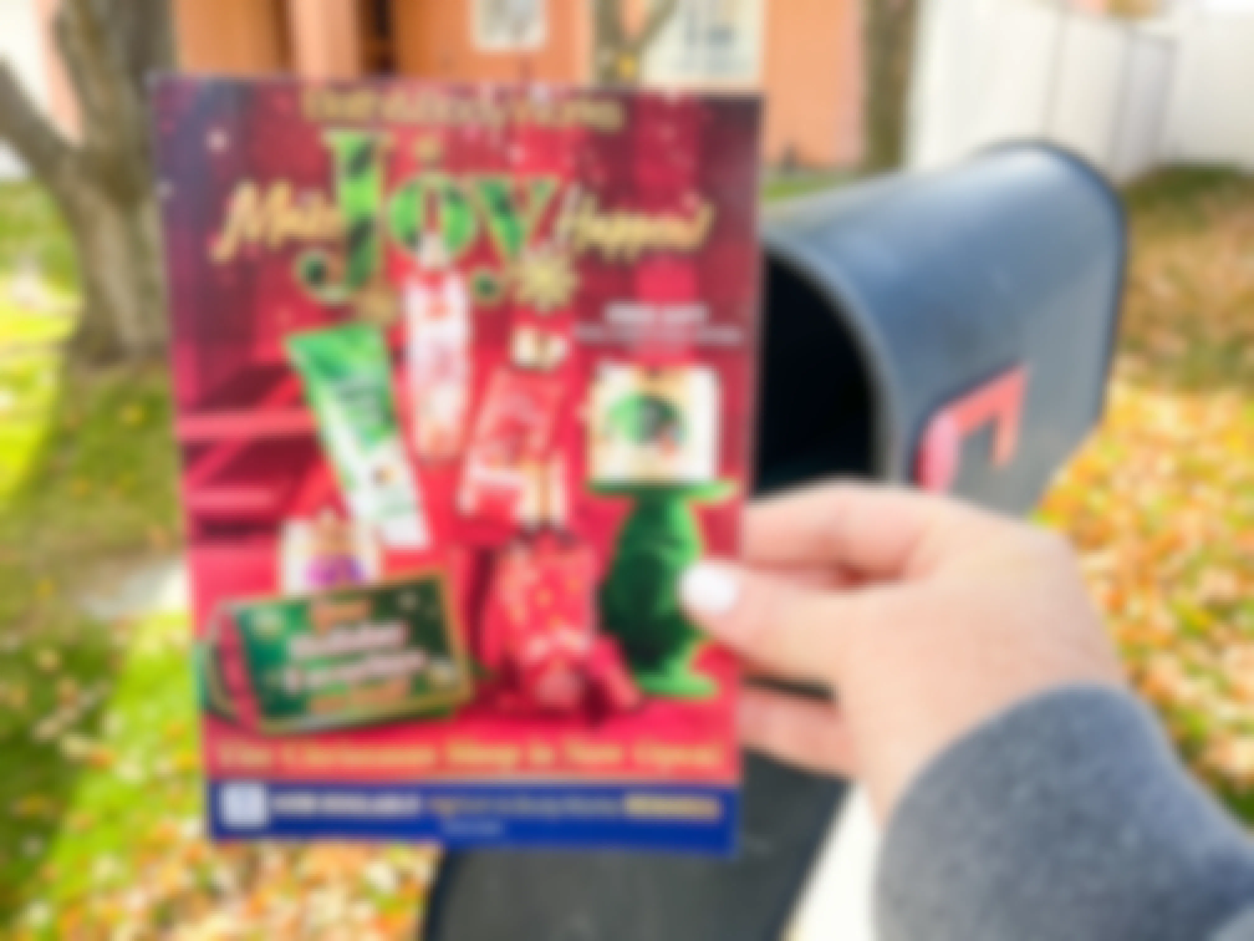 A person holding a Bath & Body Works coupon mailer next to a mail box