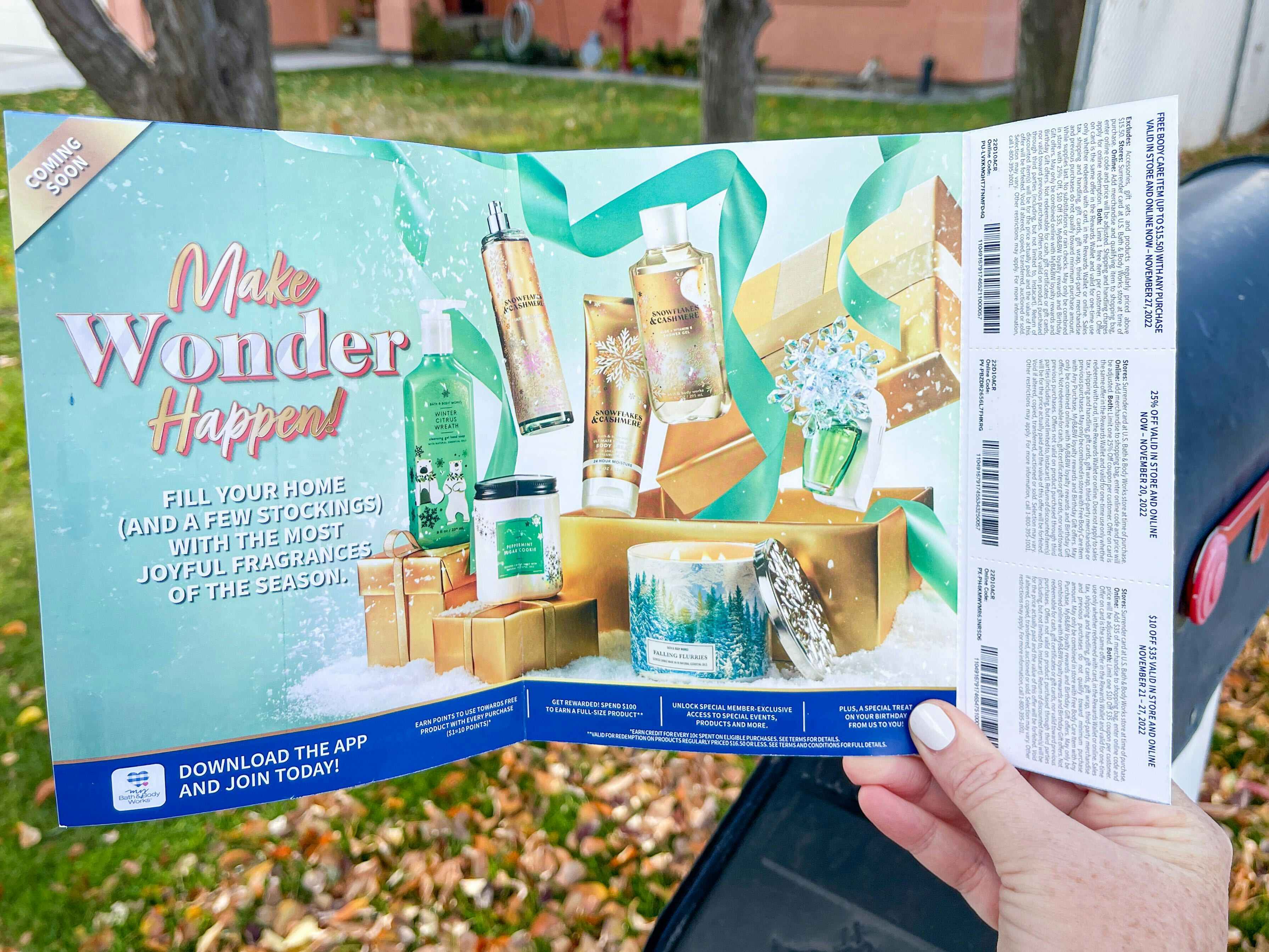 A person holding a Bath & Body Works coupon mailer next to a mail box