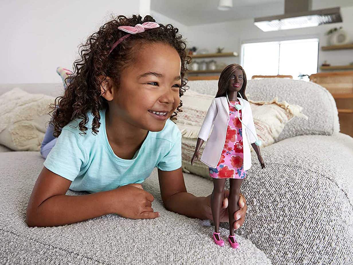 young girl playing with barbie doctor doll at home