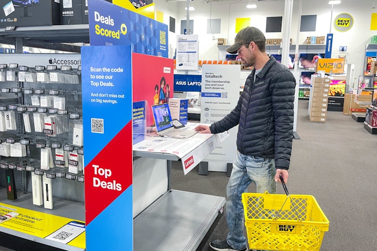 a person looking at a laptop by a top deals sign in best buy