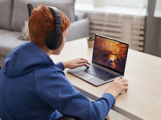 A teenager playing a video game on a laptop.