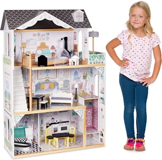 A child standing next to a Lil' Jumbl Kids Wooden Dollhouse