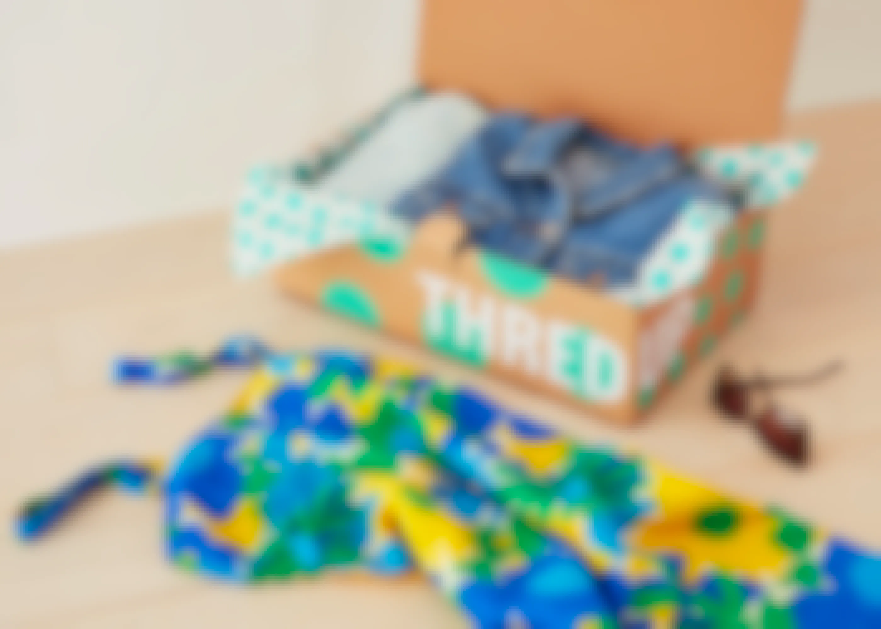 A ThredUp box with a denim jacket inside and some sunglasses and a dress on the table beside the box.