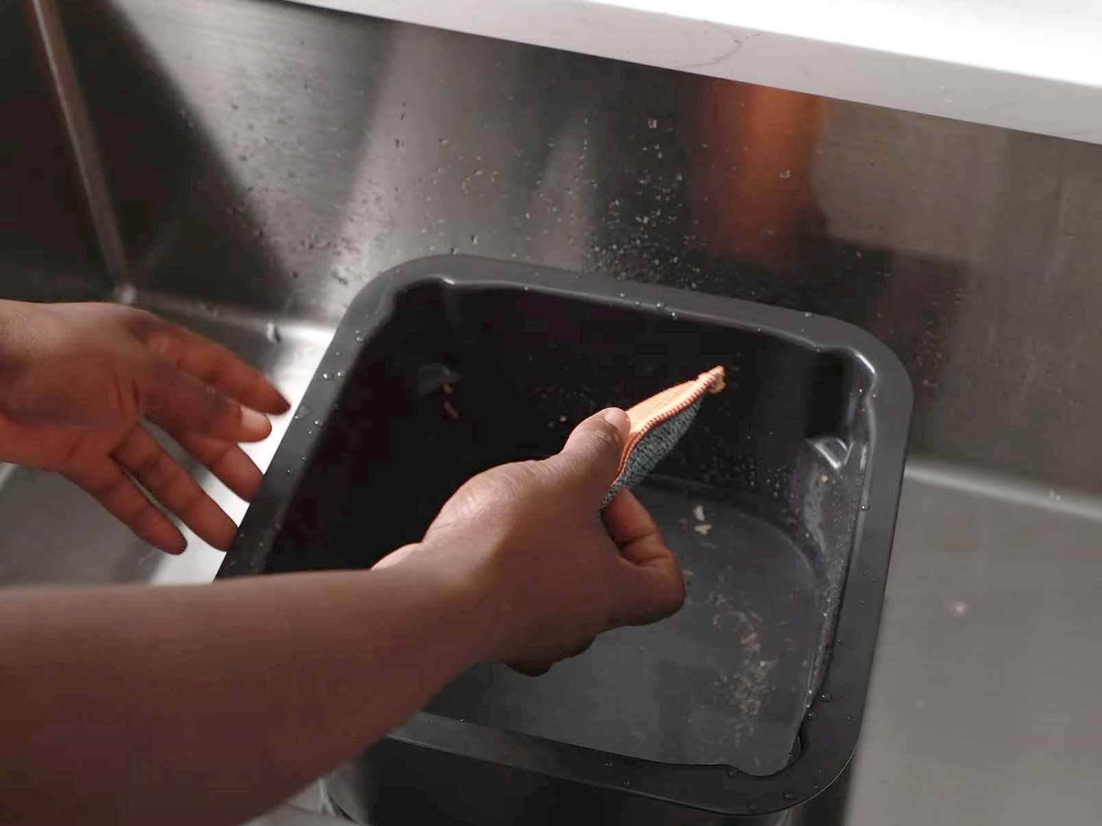 person wiping ninja air fryer basket with water and sponge