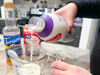 a person using milk, syrup and cream with electric frothier to create cold foam for iced coffee
