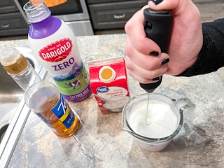 a person using milk, syrup and cream with electric frothier to create cold foam for iced coffee