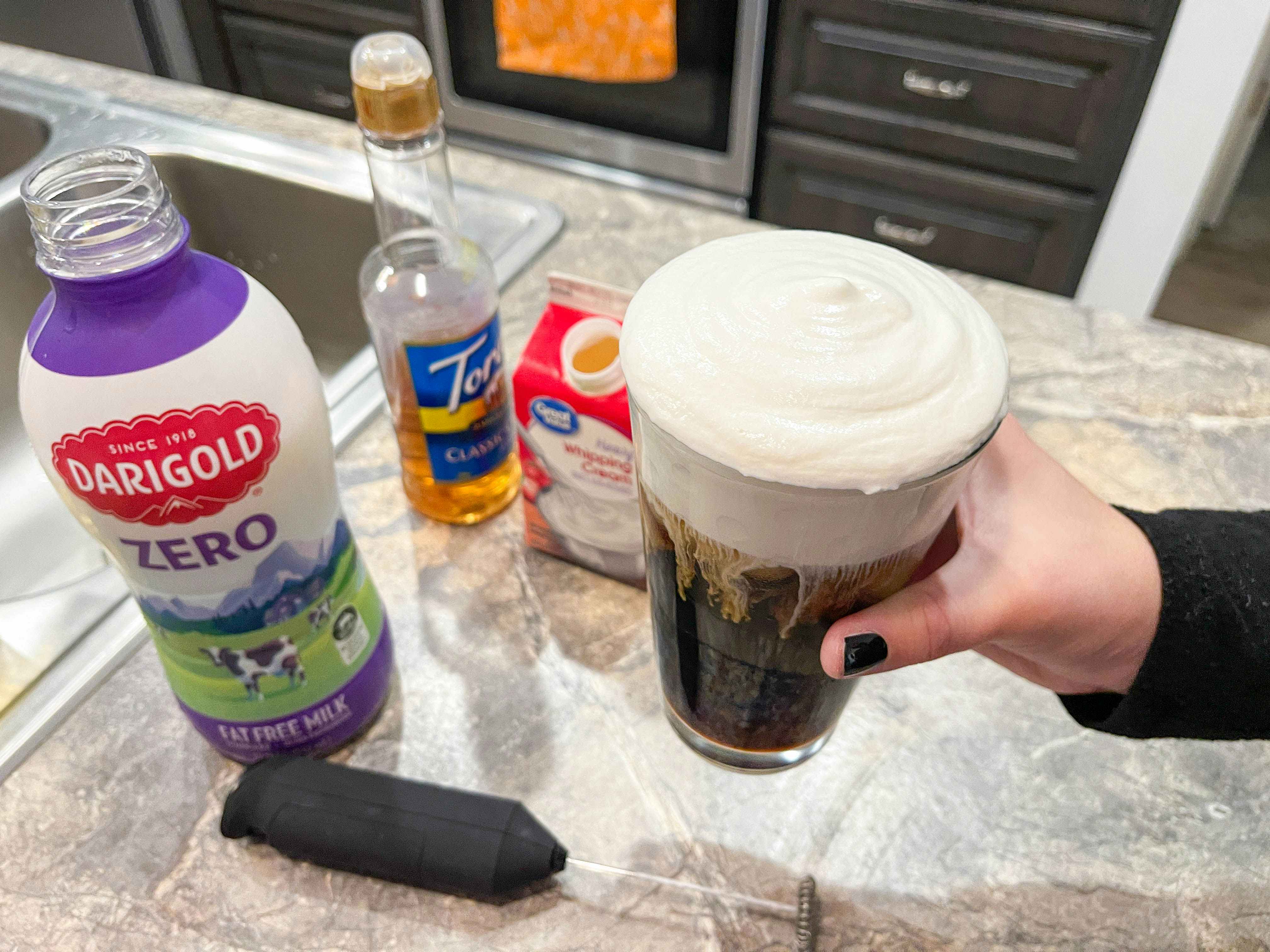 a person using milk, syrup and cream with electric frothier to create cold foam for iced coffee