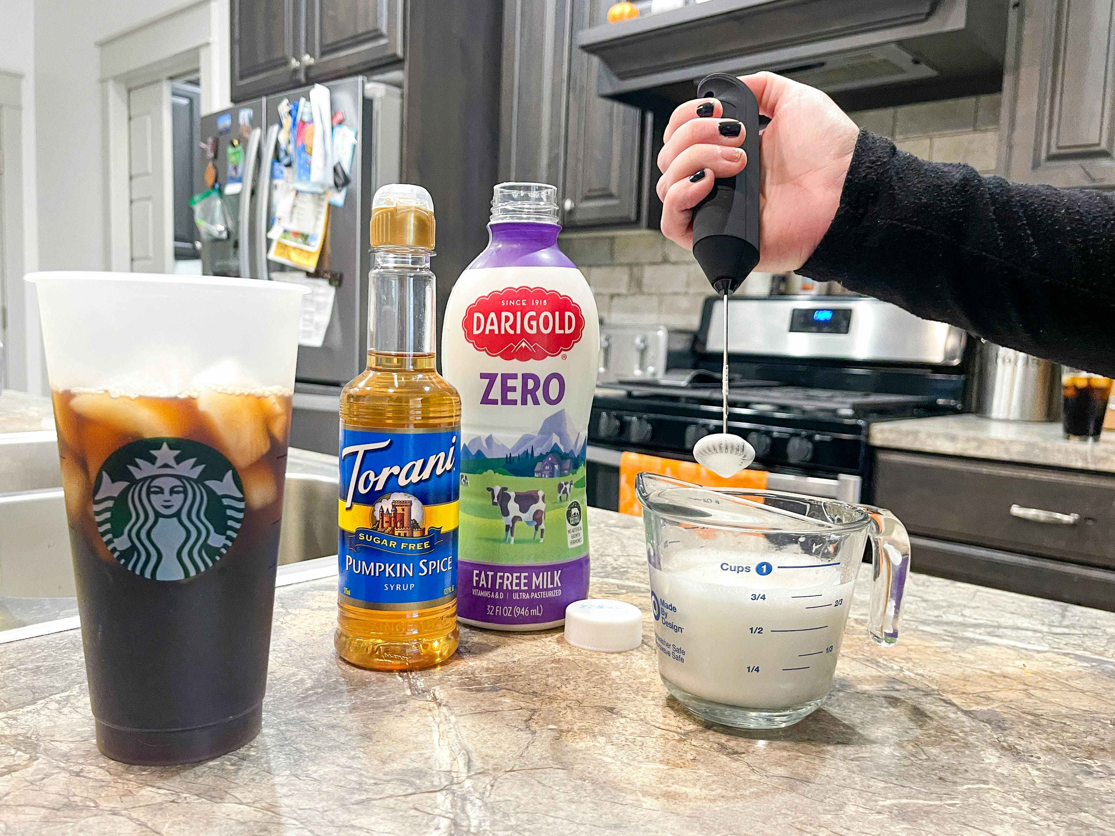a person using milk, syrup and cream with electric frothier to create cold foam for iced coffee