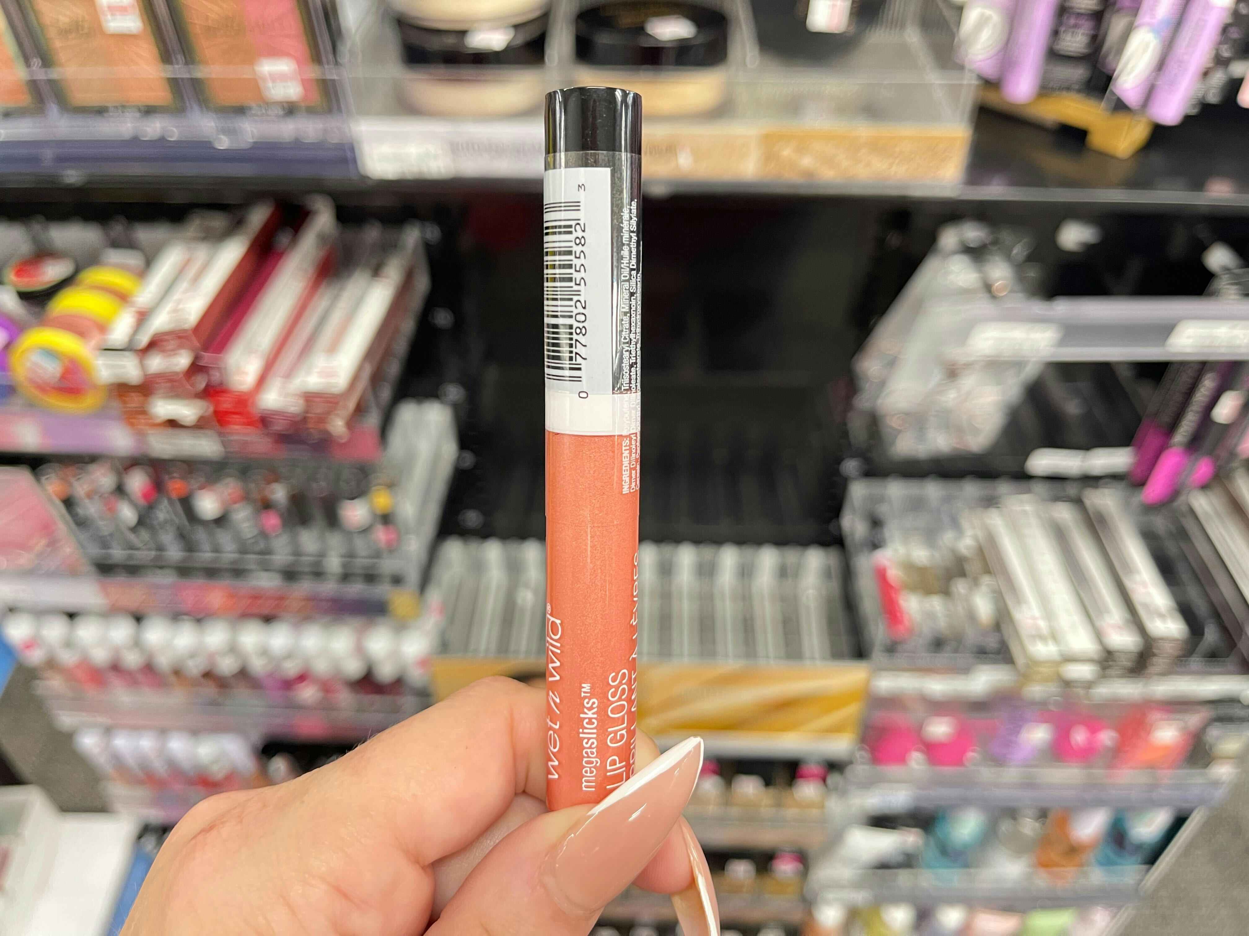 hand holding Wet n Wild megaslicks lip gloss in front of product display
