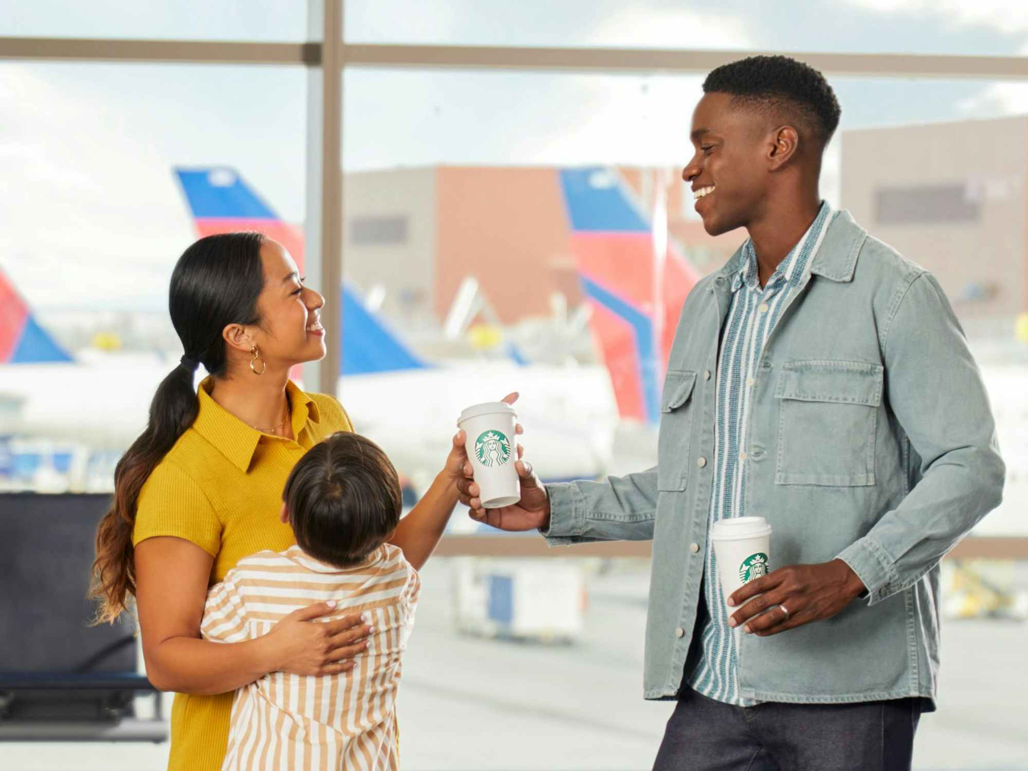 a family in an airport in front of some Delta planes holding Starbucks cups