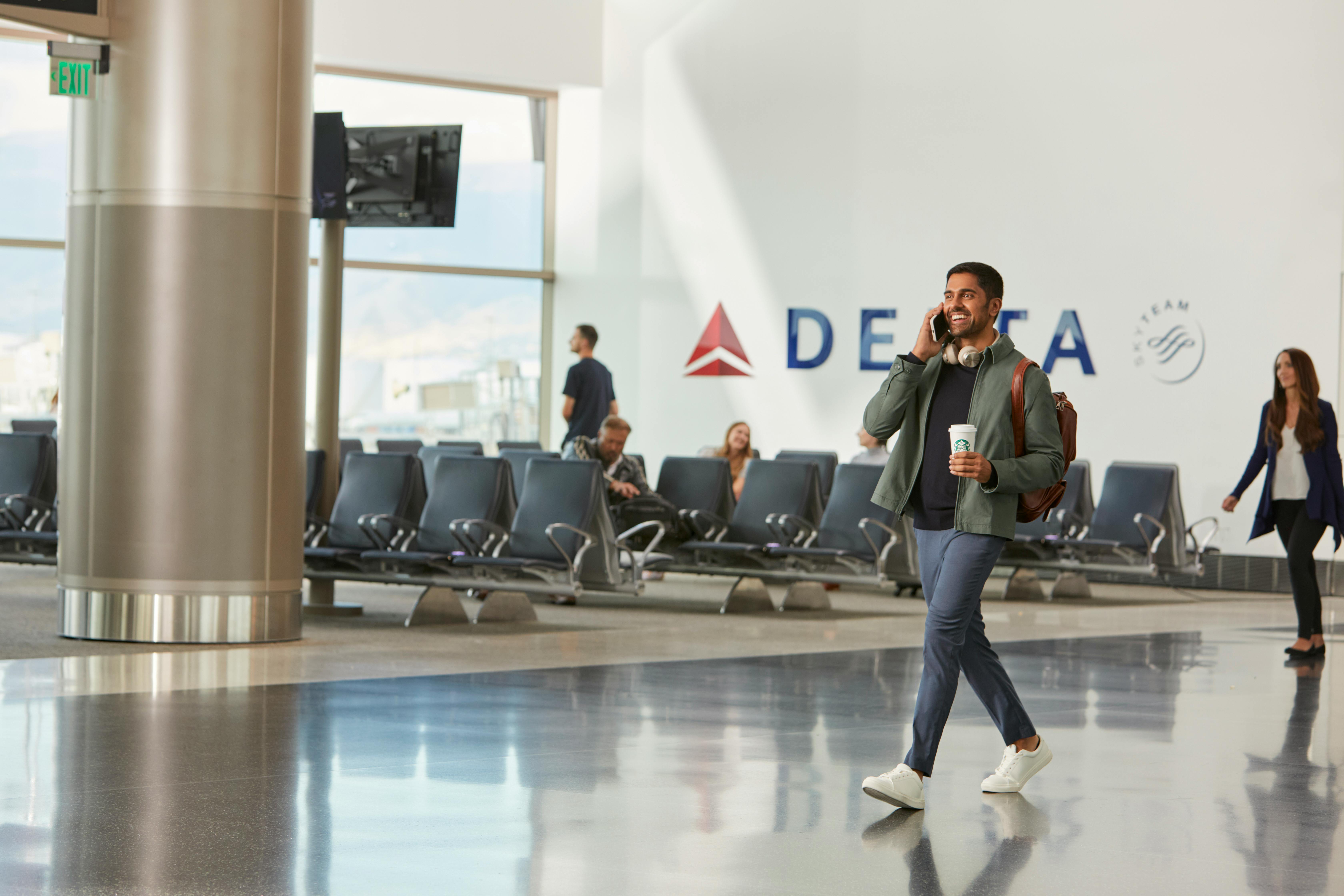 Man walking in an airport with Starbucks cup in hand, in front of a Delta sign