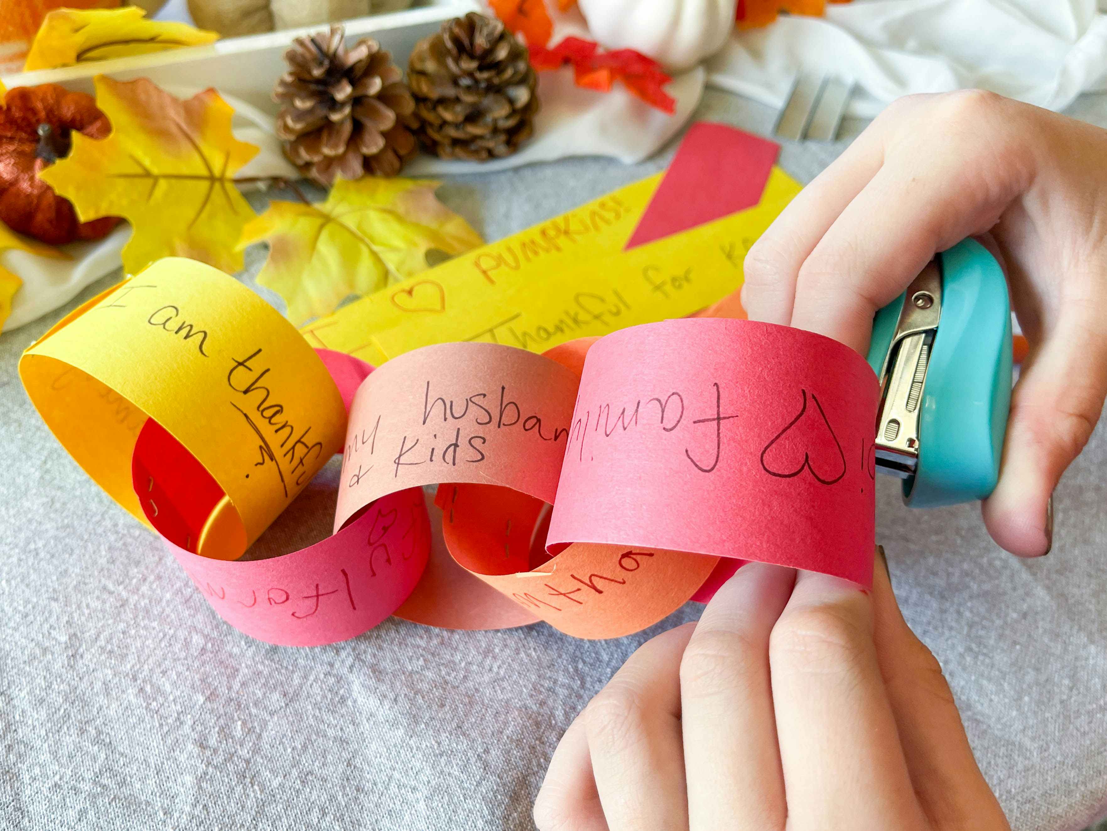 a person stapling pieces of cut paper to make a chain of written thankful notes