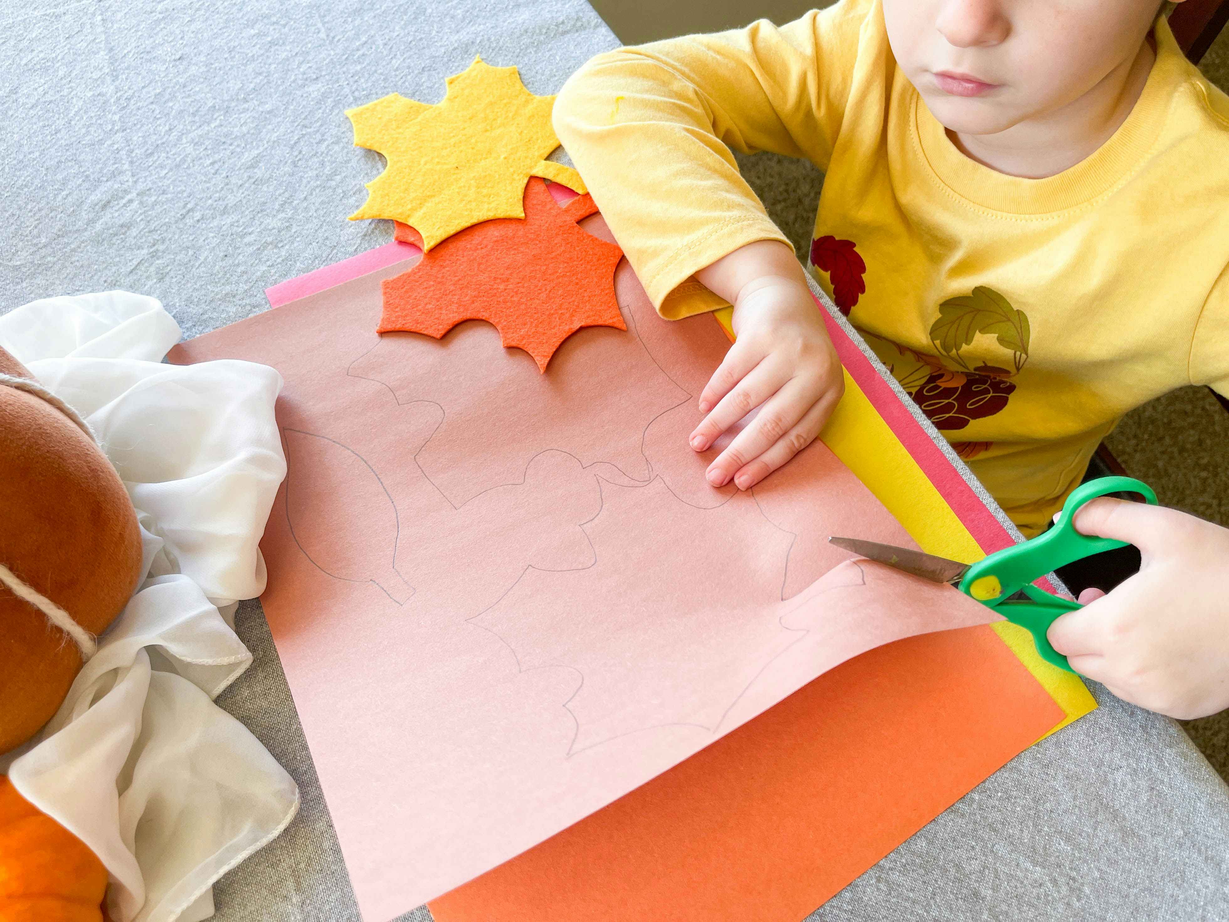 a young child cutting leaf shapes out of construction paper