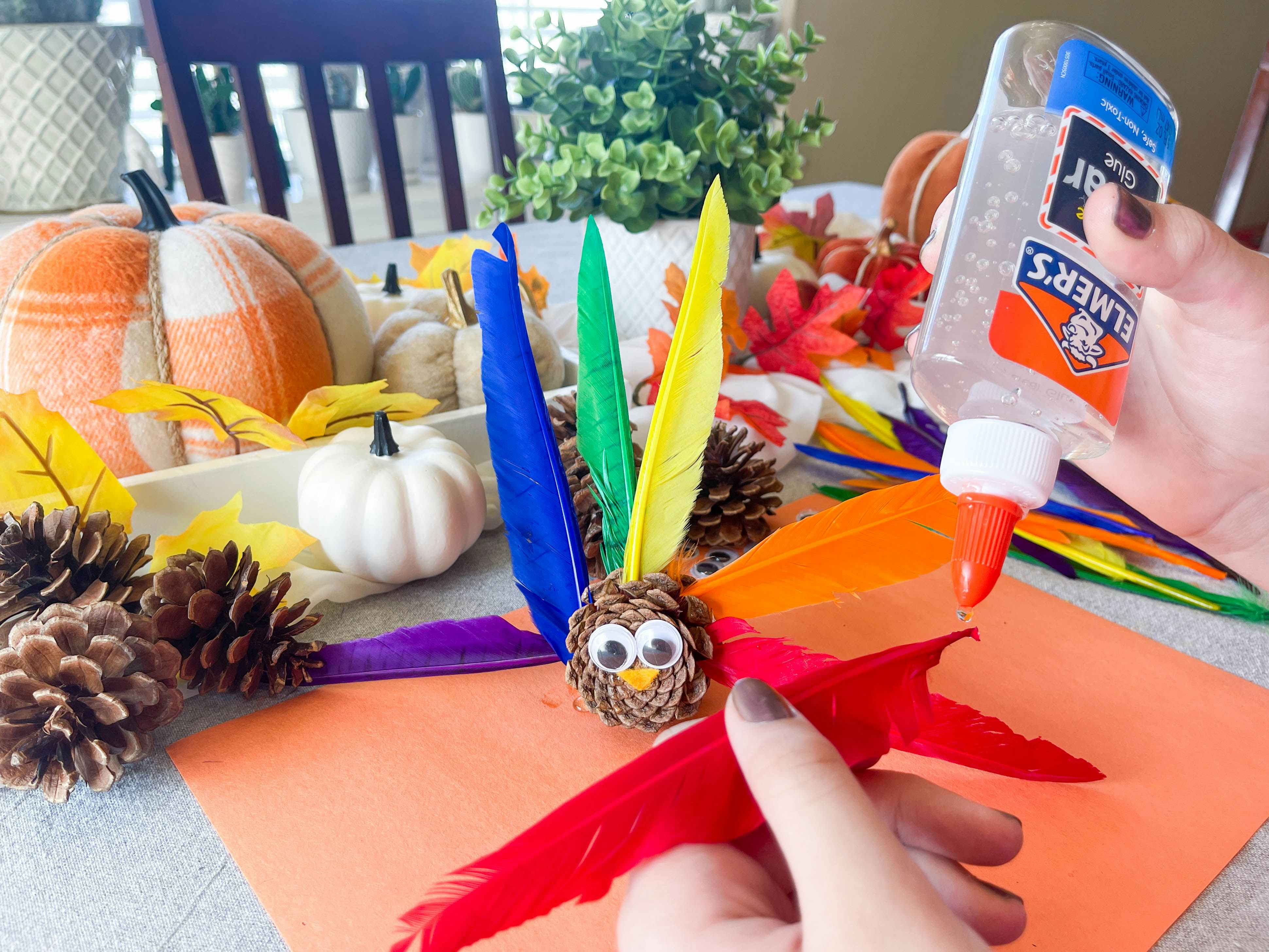 a person gluing feathers on a diy pinecone turkey