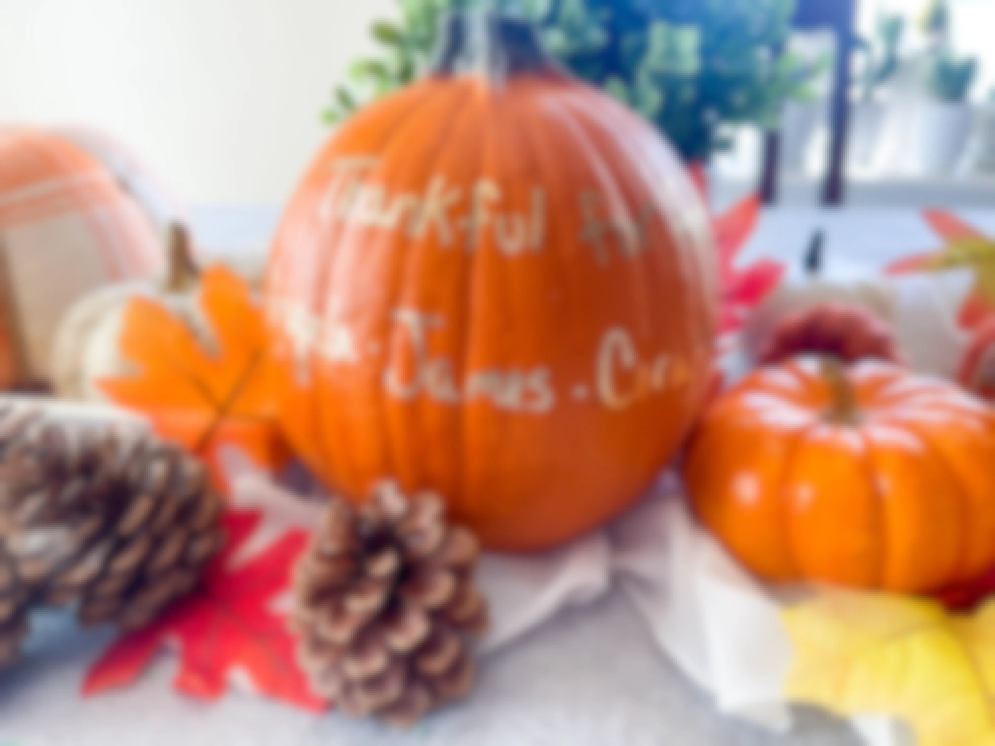 thankful message and names written in metallic pen on a pumpkin sitting on a table