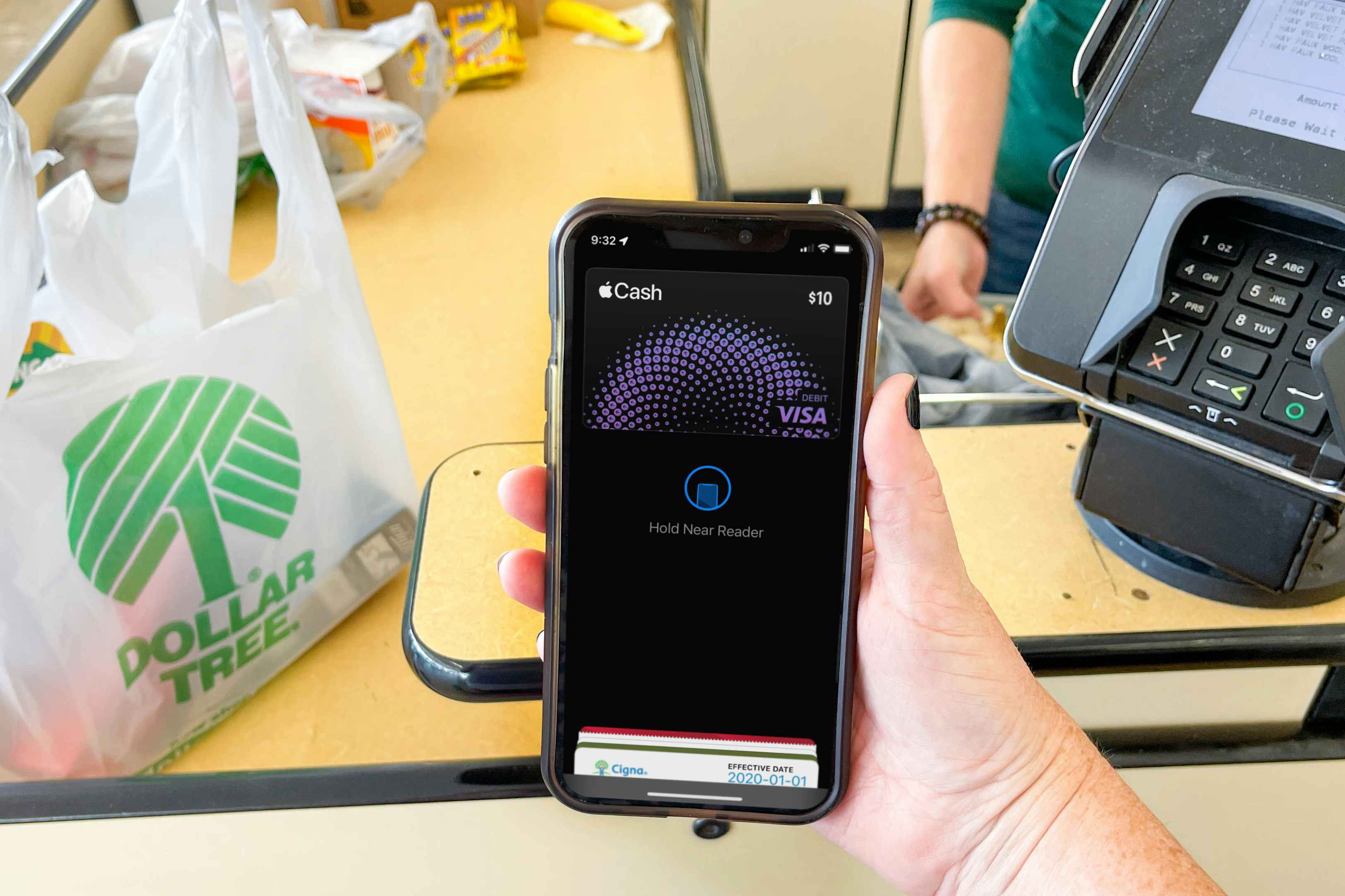 A person's hand holding a cellphone with apple pay on screen at the dollar tree register about to pay.