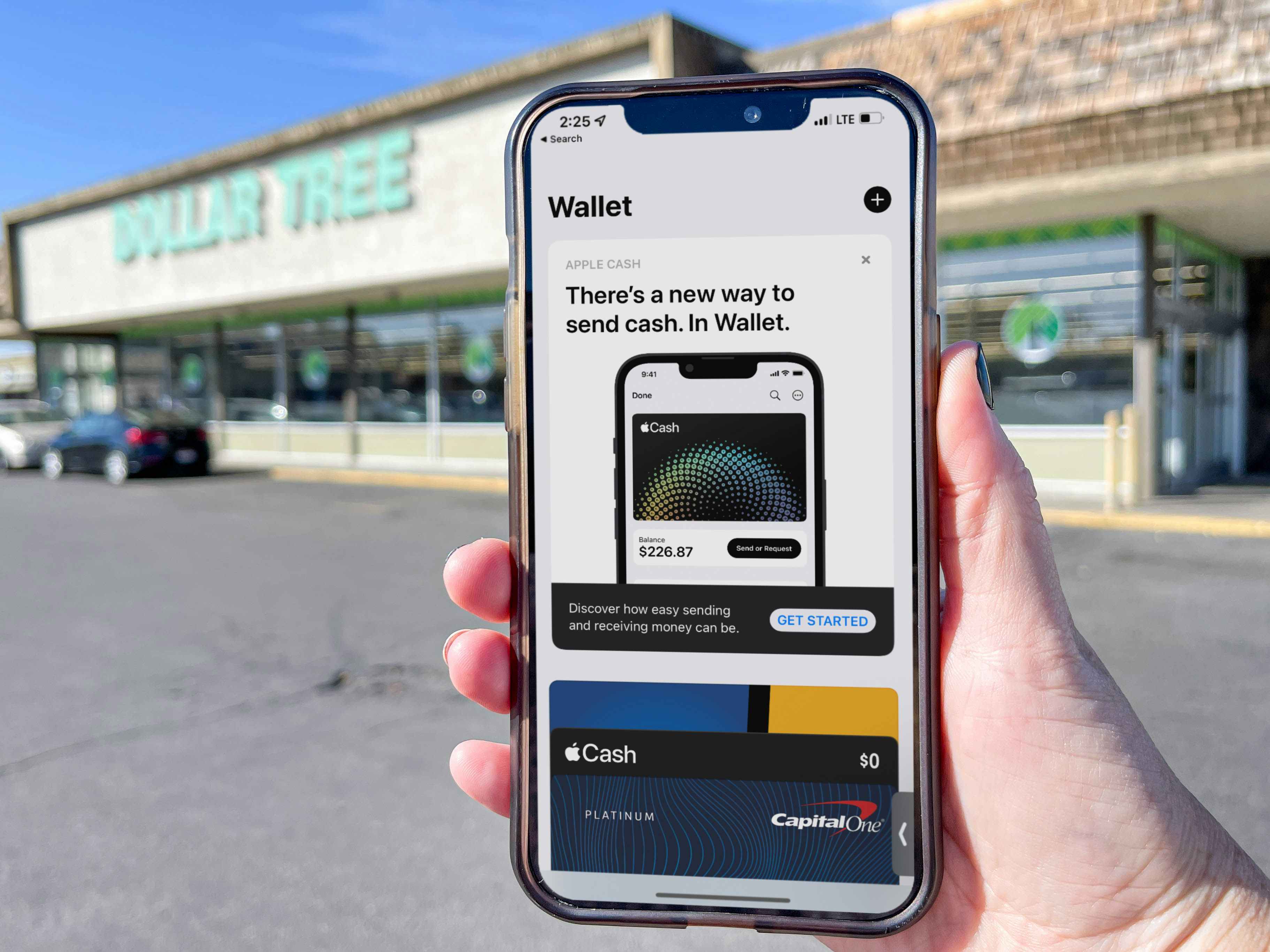 A person's hand holding a cellphone with apple pay wallet on screen in front of dollar tree.