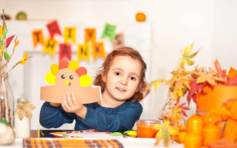 a little child holding up a paper turkey head crown