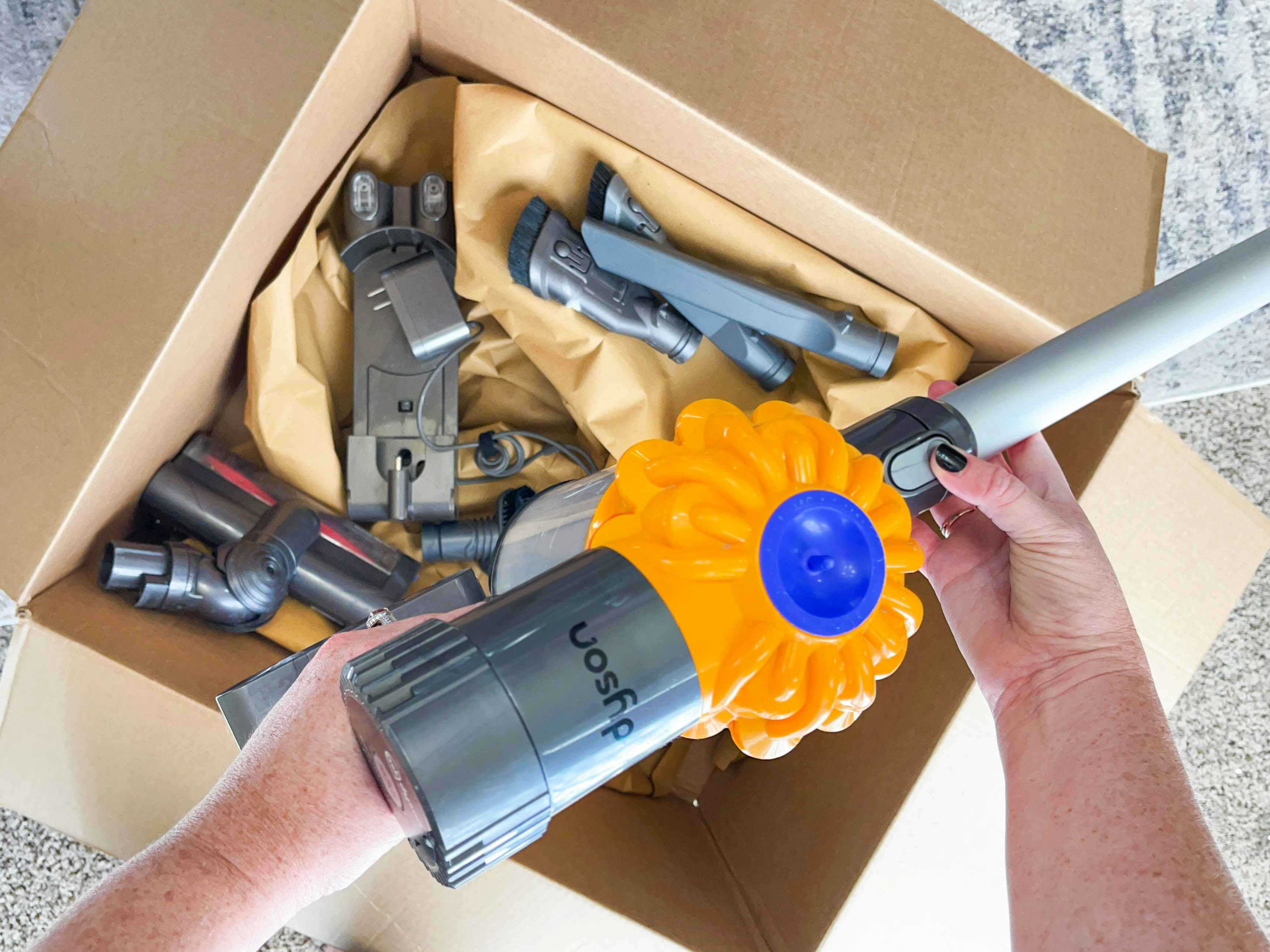 a person's hands putting together a dyson vacuum together from parts in a box on the ground