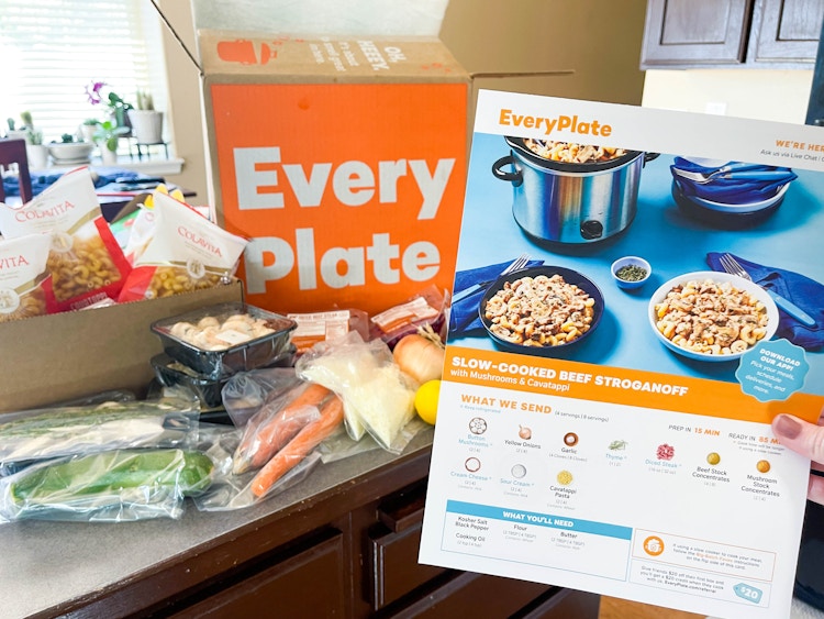 a person's hand holding up menu recipe cards in front of every plate box and food on counter