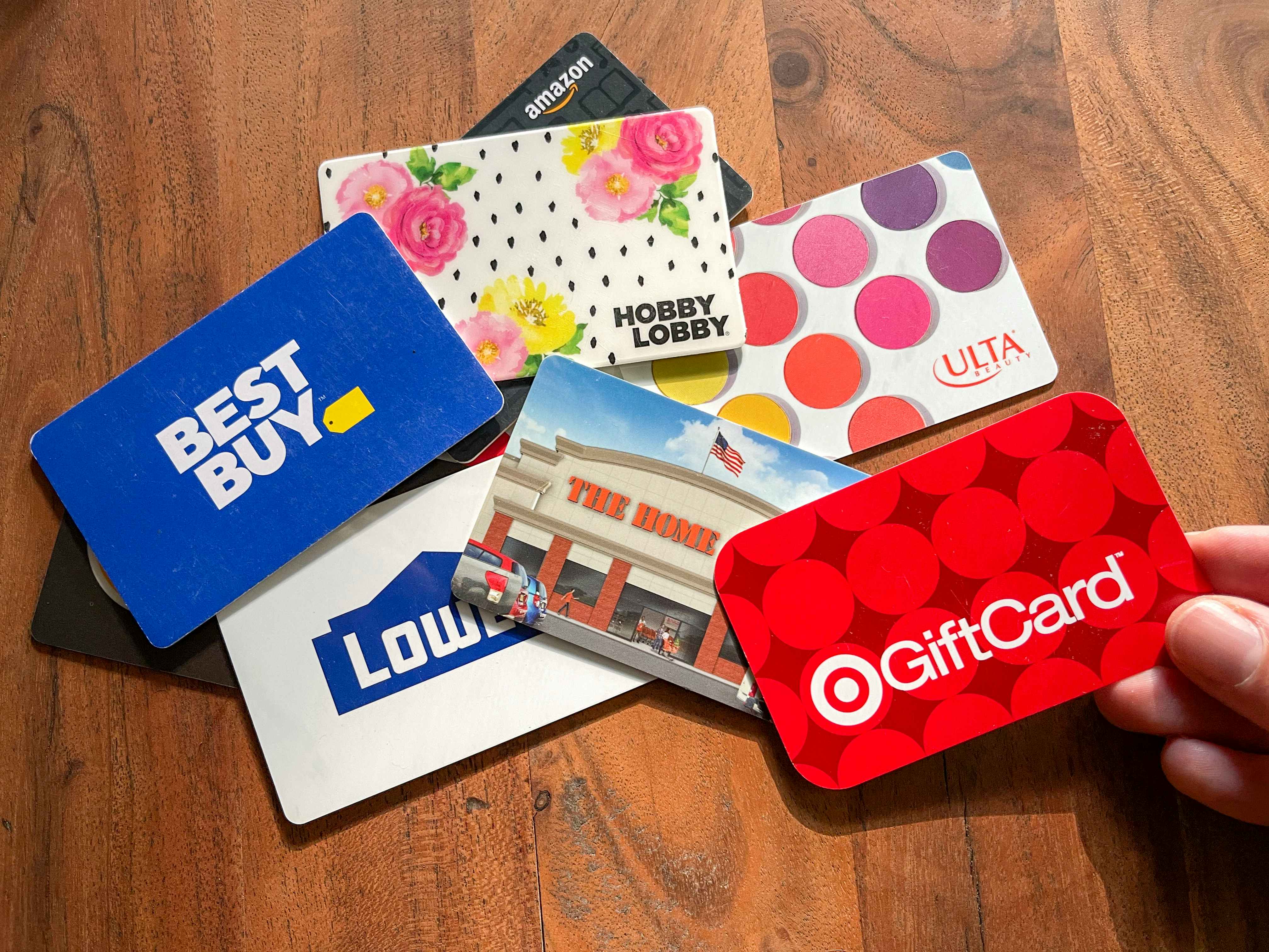 A person holding a target gift card with a bunch of other gift cards on the table behind it.